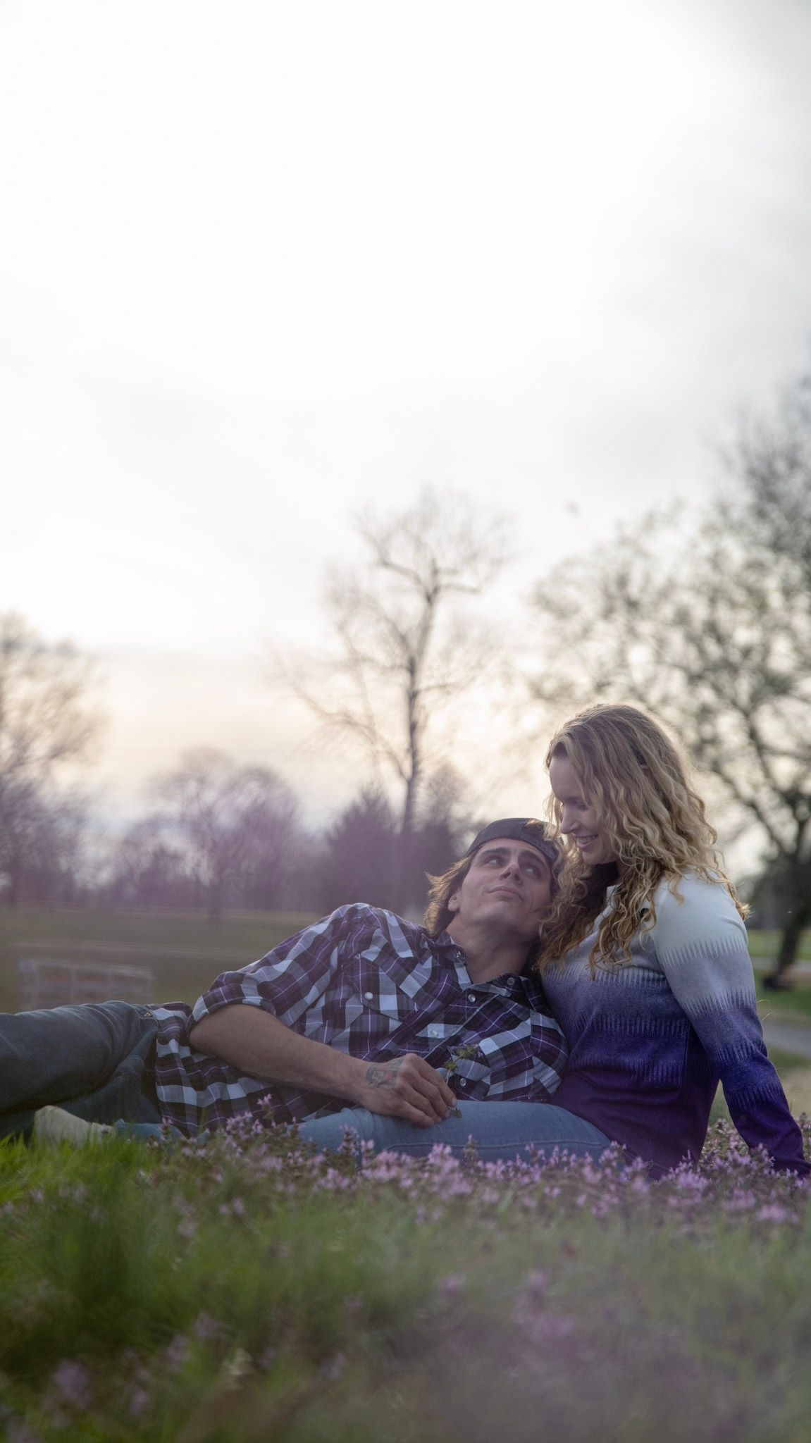 Couple lying in a field of purple flowers during sunset.