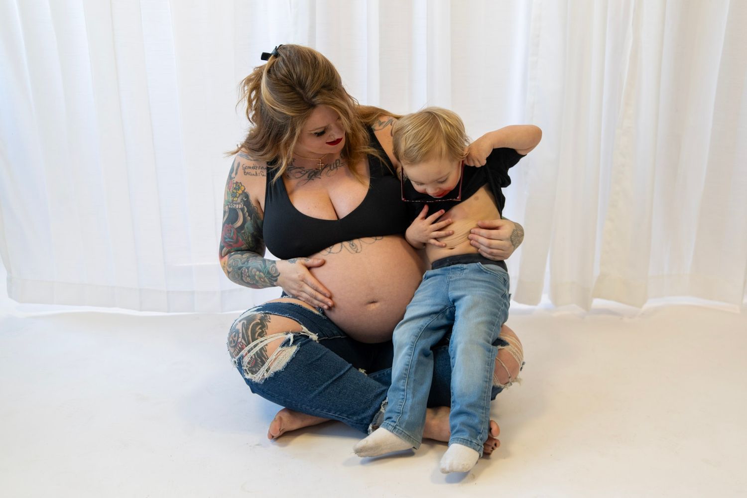 Family sharing intimate moments during pregnancy photo session against white backdrop.