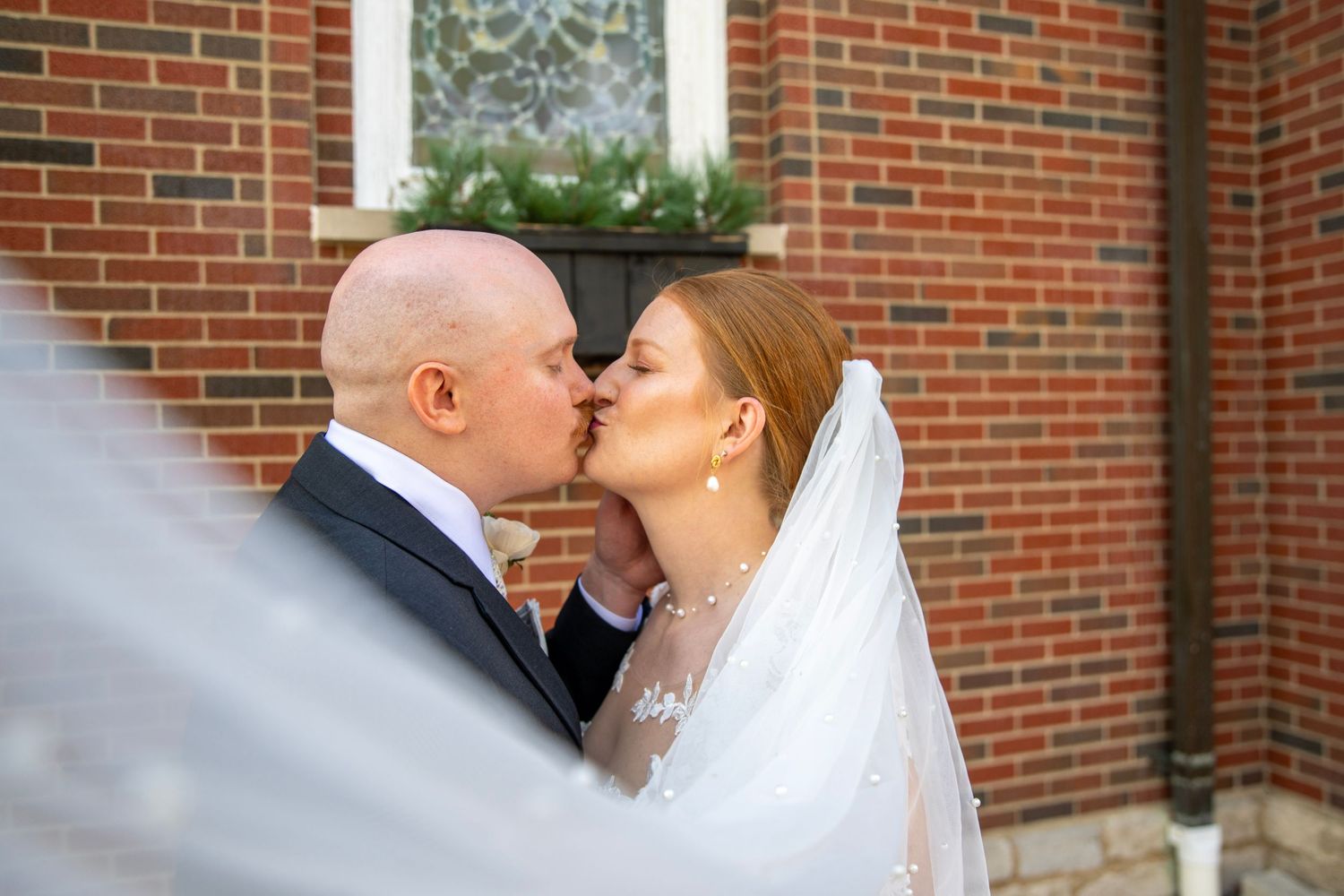 A tender kiss shared between newlyweds against a brick building backdrop.