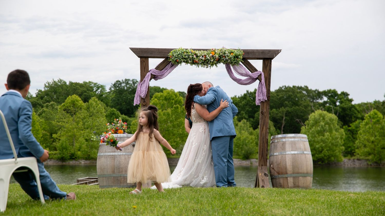 Panoramic view of a lakeside wedding ceremony with wooden arch and rustic barrels.