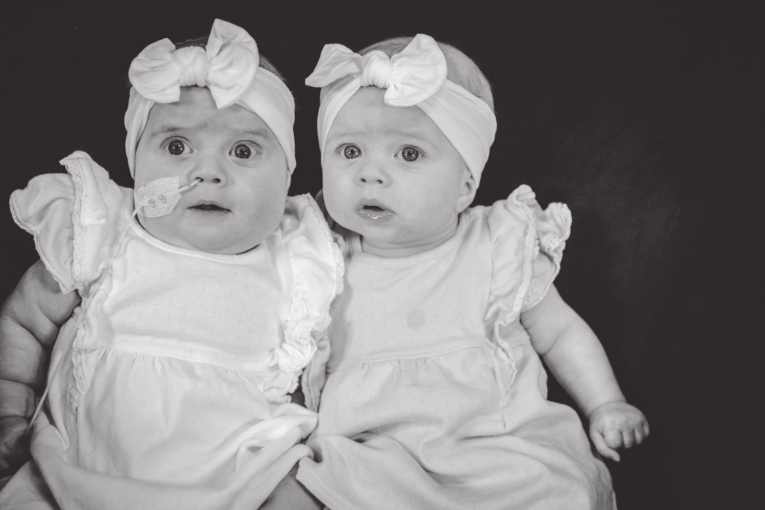 Black and white portrait of twin babies in matching white outfits.