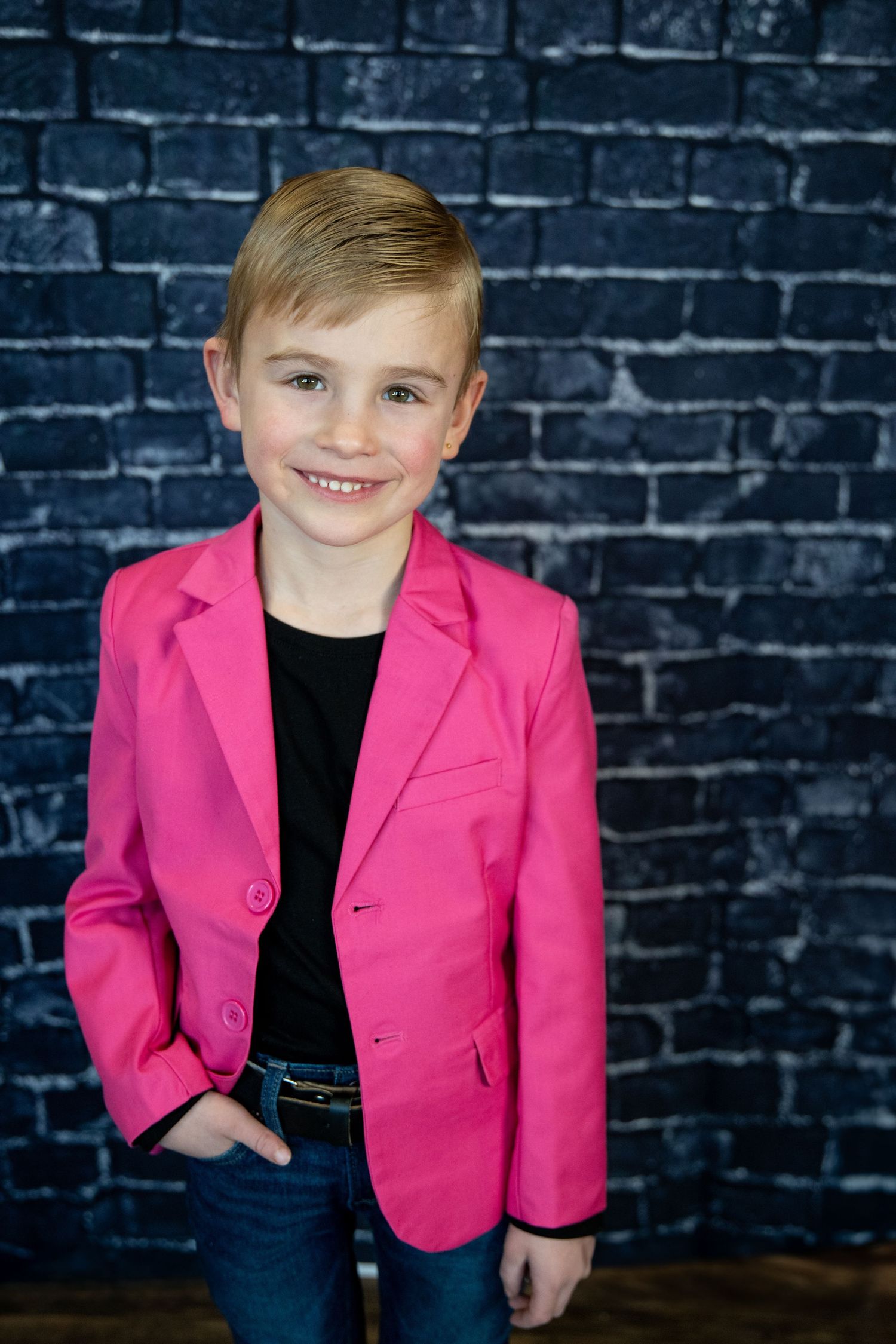 A stylish outfit featuring a hot pink blazer and black top posed against blue brick.