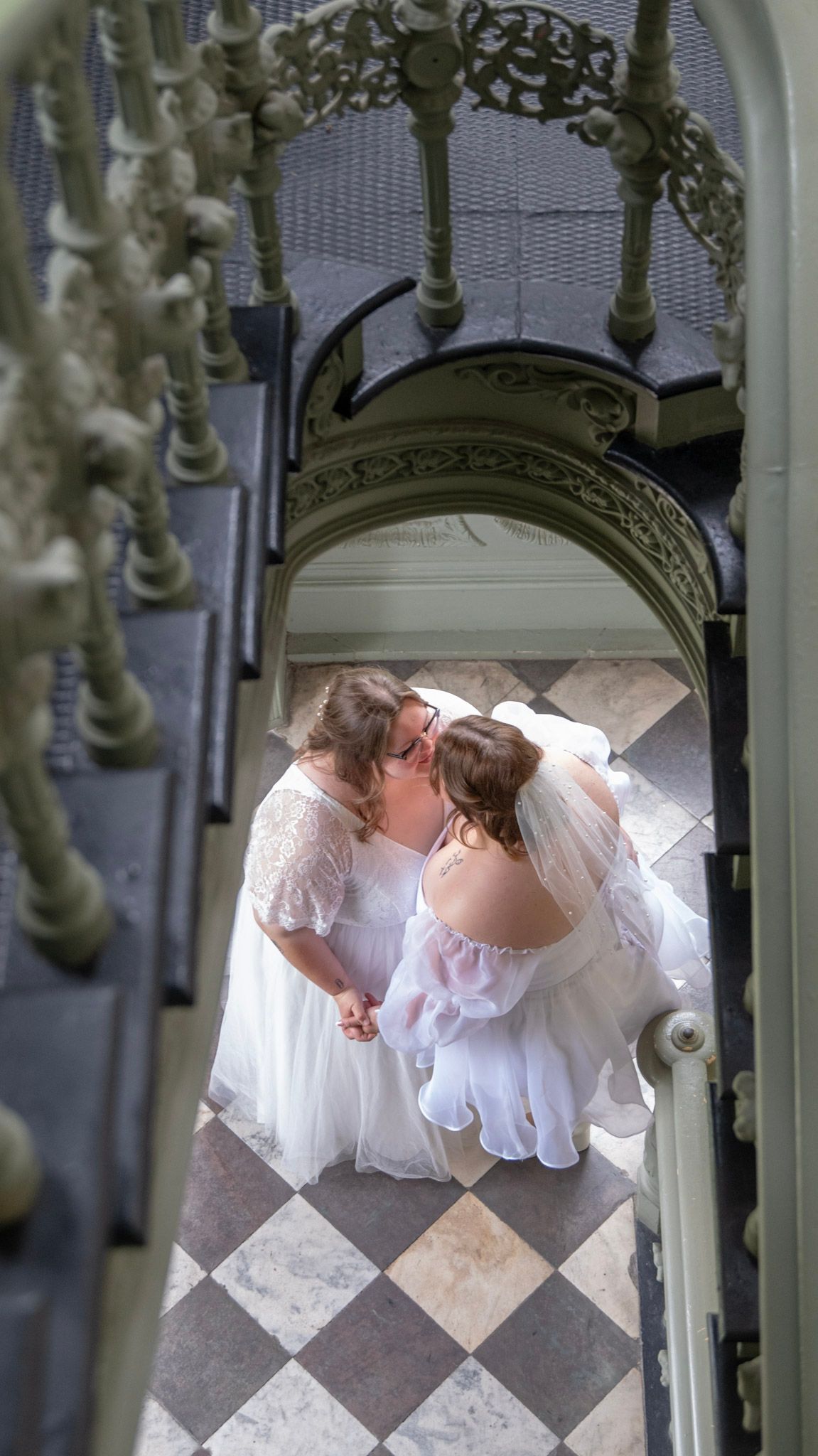 Artistic overhead shot of wedding couple on checkered floor through ornate railing.