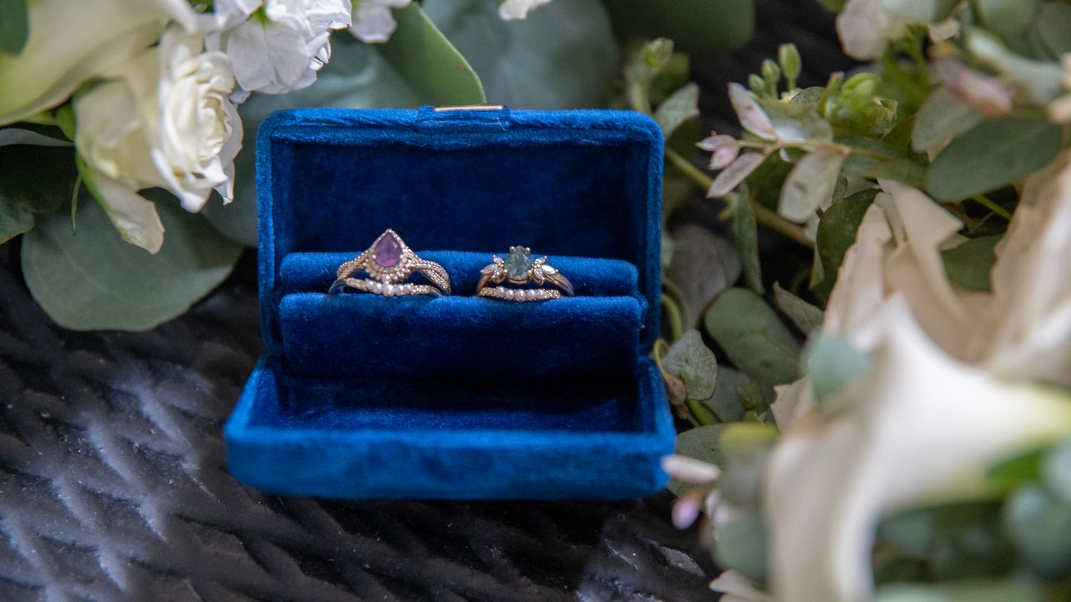 Blue velvet ring boxes displayed among white floral arrangements and greenery.