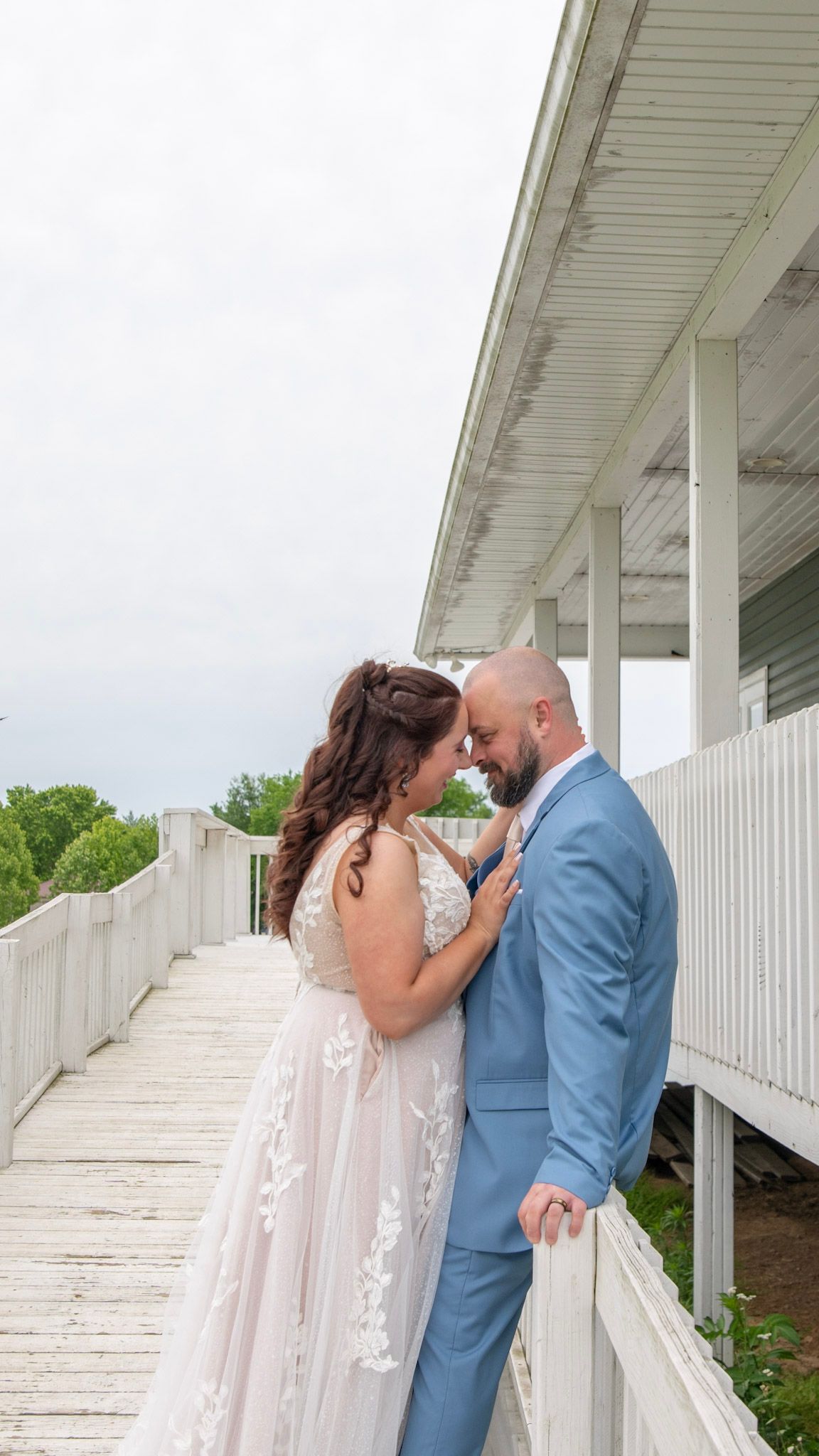 A couple in wedding attire share an intimate moment against a white fence backdrop.