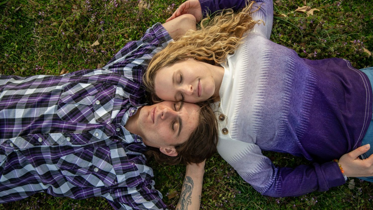 A couple lying on a plaid blanket in the grass sharing a tender moment together.