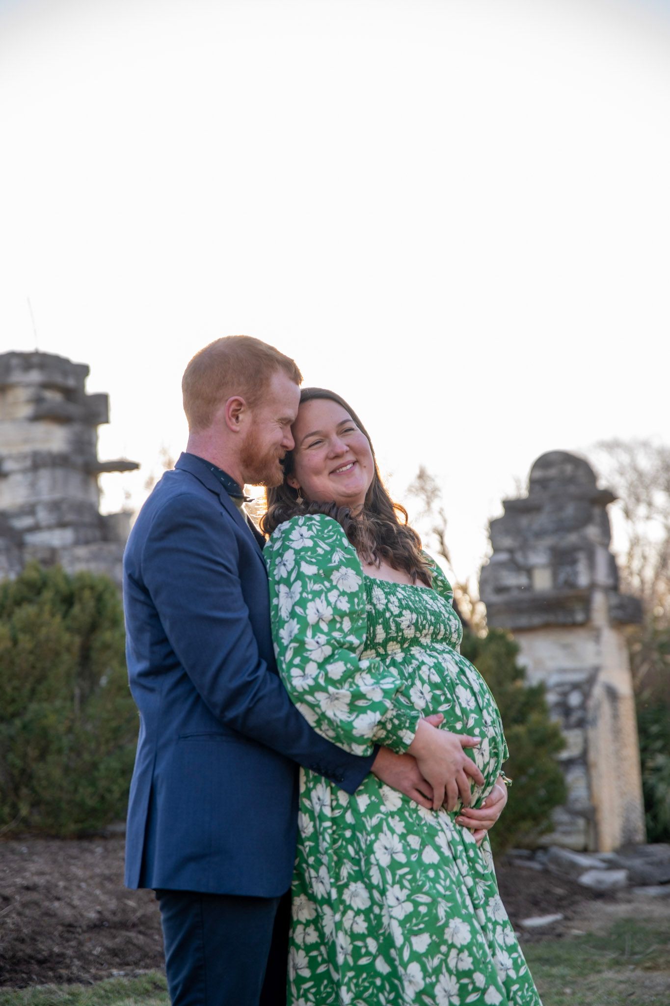 A romantic outdoor photoshoot featuring a couple in a green floral dress and navy suit.