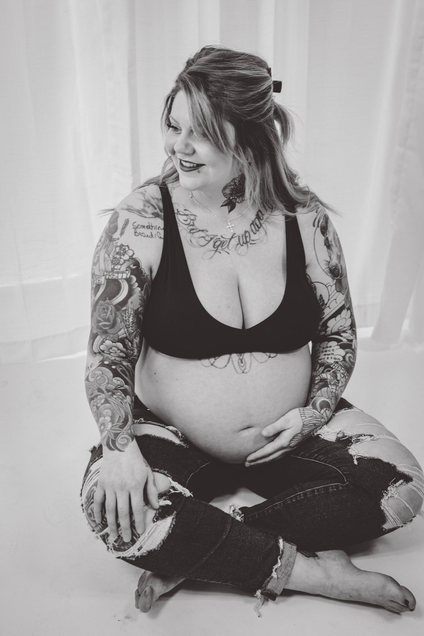 Monochrome maternity portrait featuring tattoo sleeves and casual denim attire.