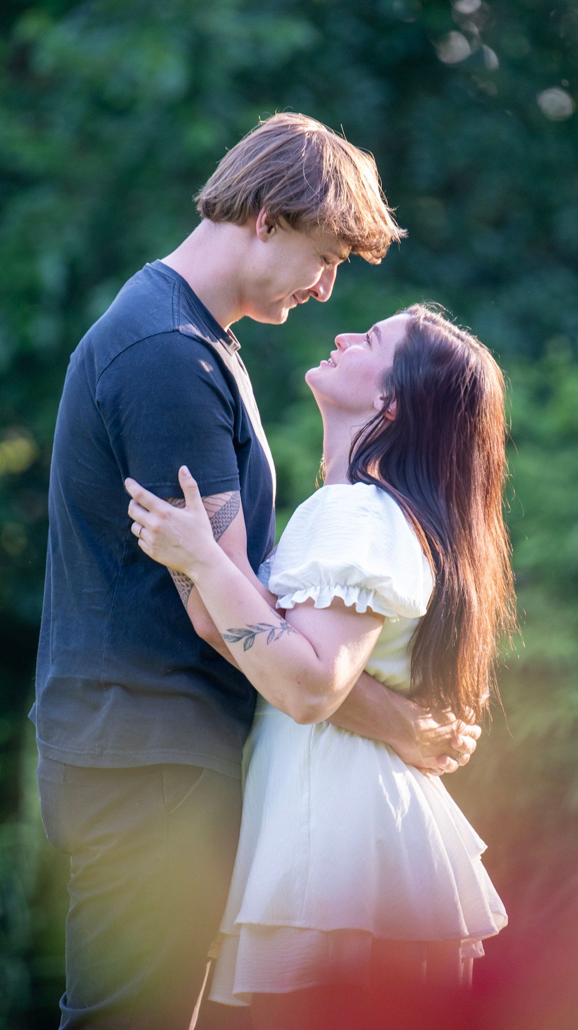 A tender moment between a couple in a white dress and dark shirt against a garden background.