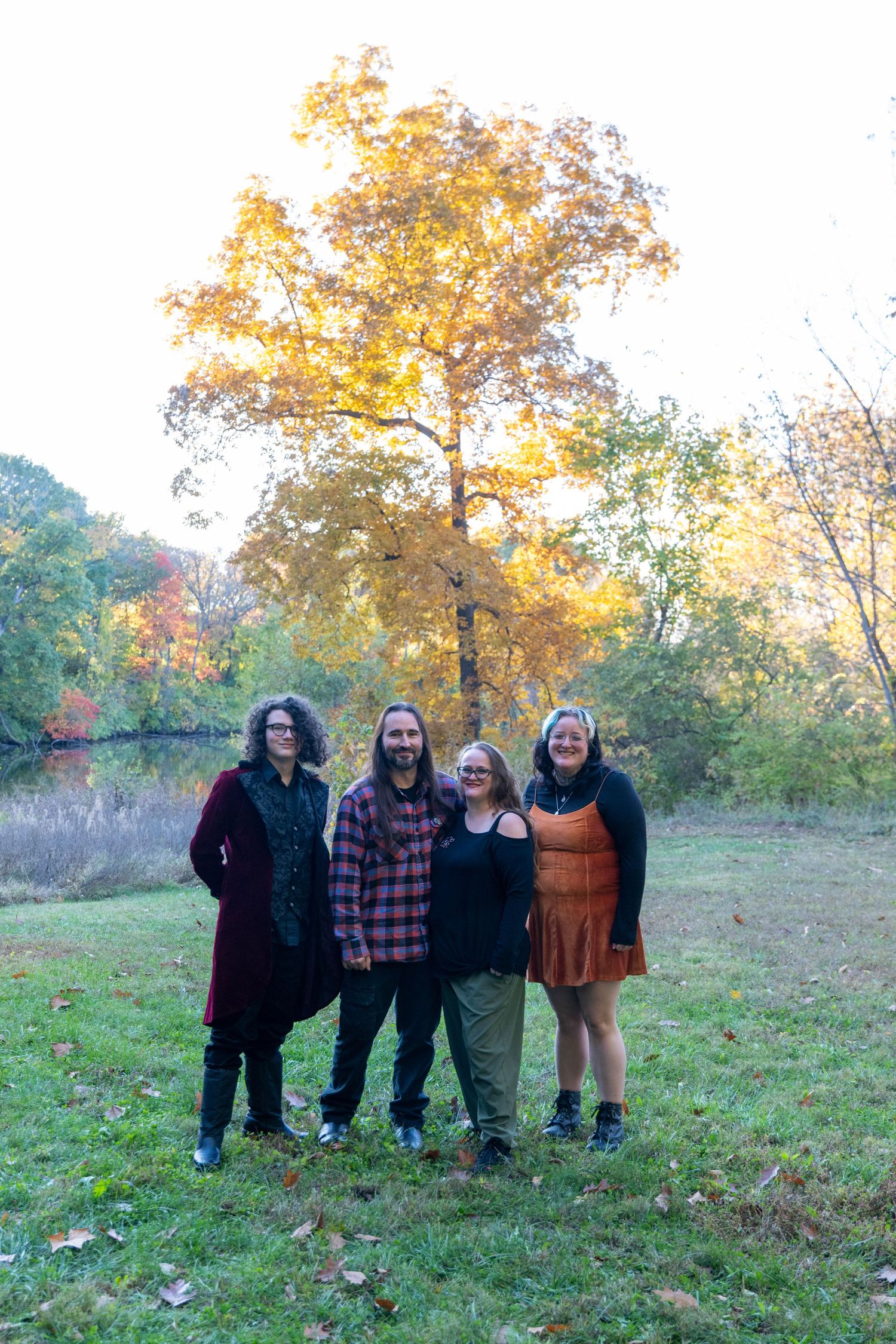 Group portrait of family members standing together on grassy hill with fall foliage behind them.
