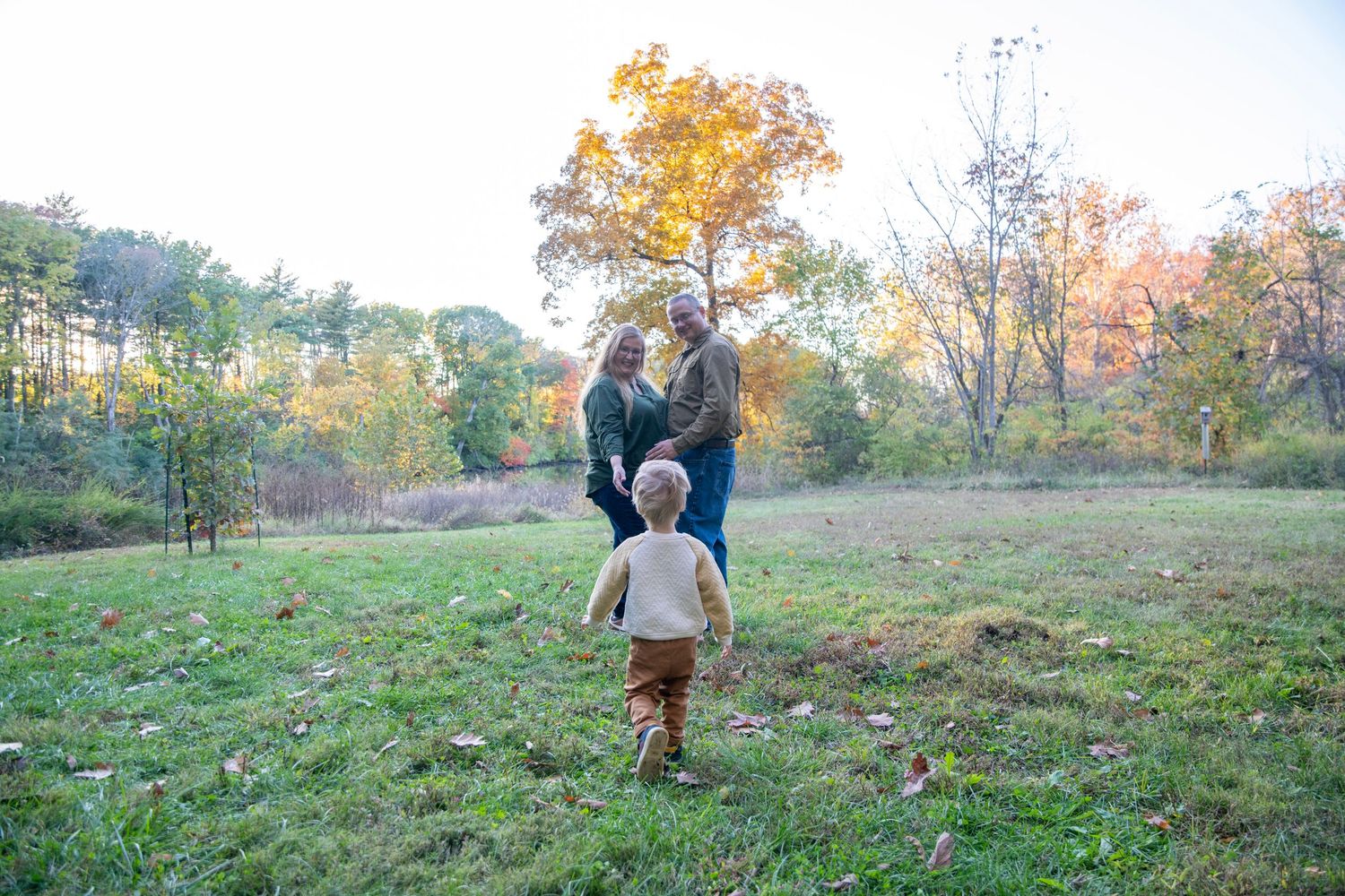 A scenic autumn landscape with people walking through a grassy field at sunset.