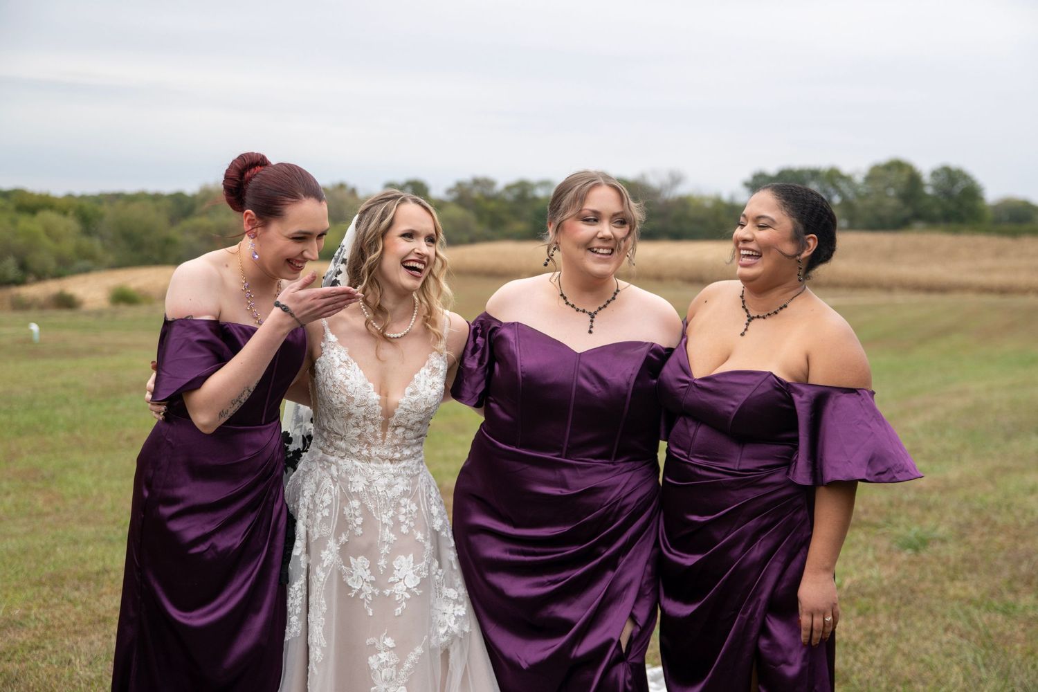 Wedding party shares a candid moment of laughter in a rustic outdoor setting.