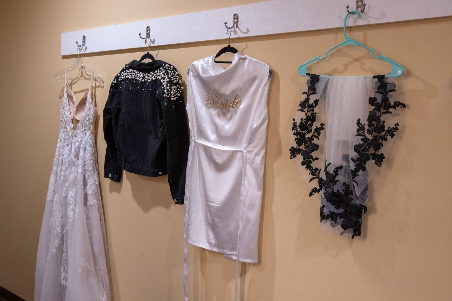 Wedding attire and accessories hanging on wall-mounted hooks in a dressing room.