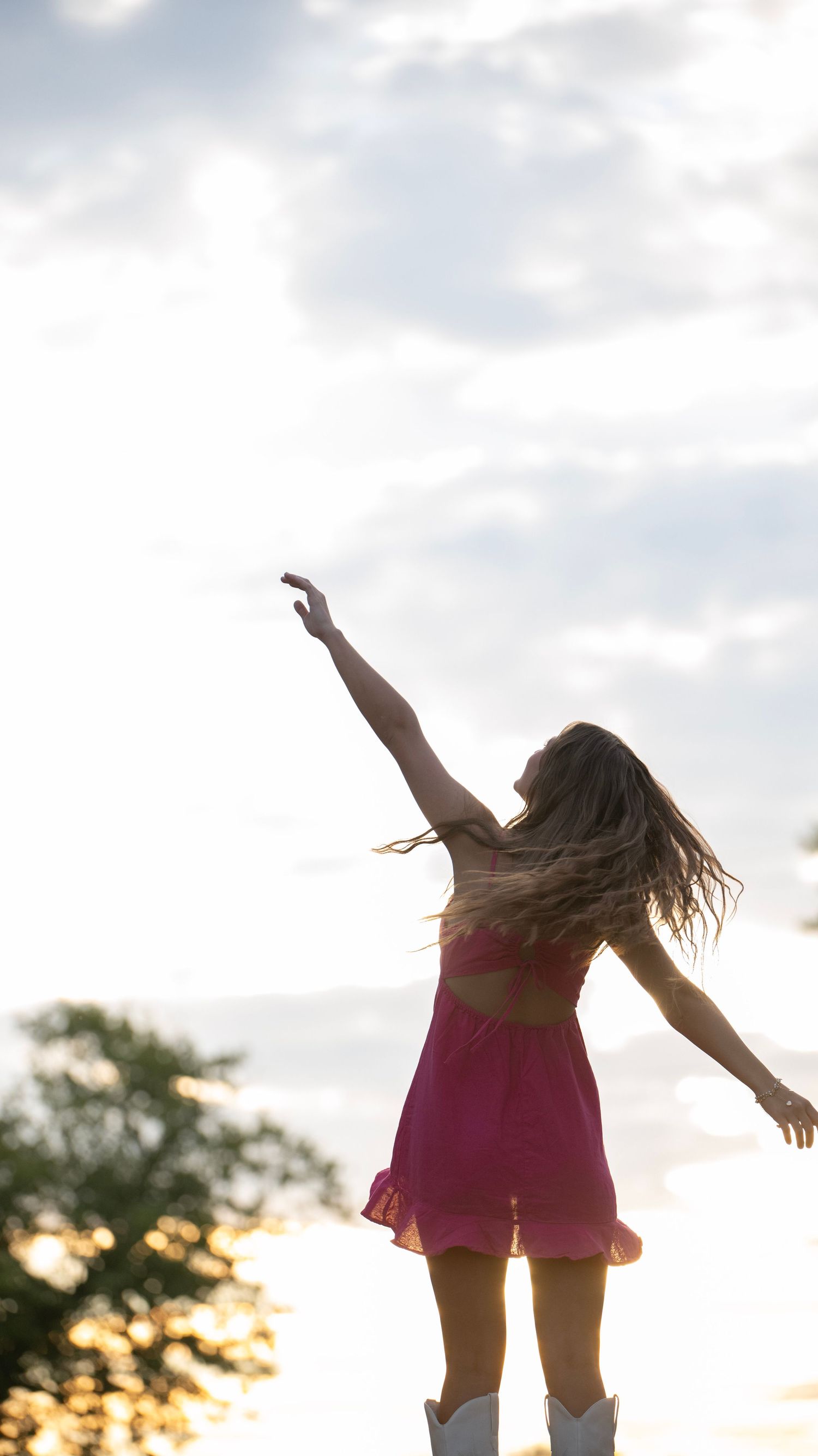 Silhouette dance pose against sunset sky in flowing dress.