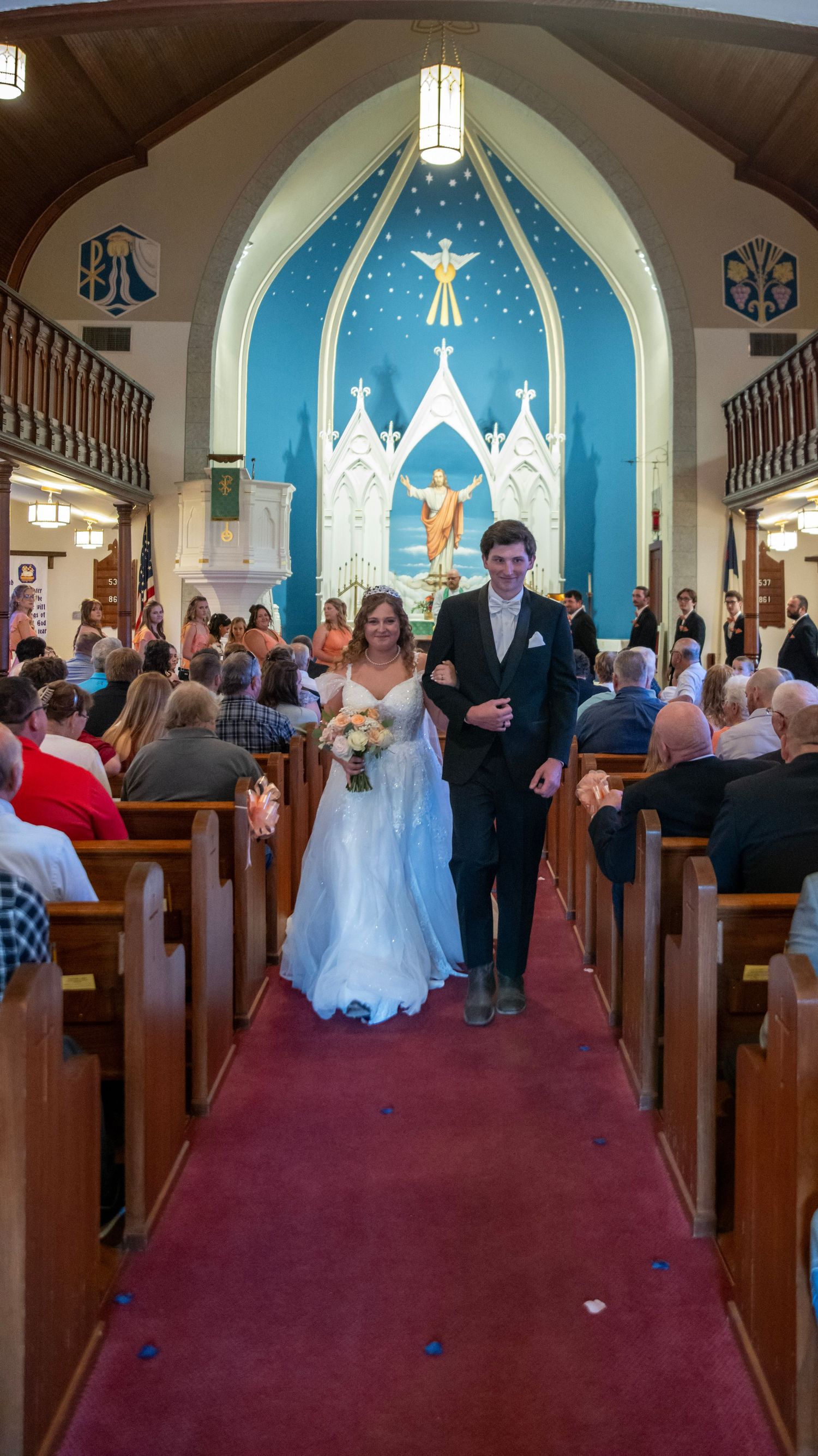 Wedding ceremony procession in a church with blue altar backdrop and filled pews.