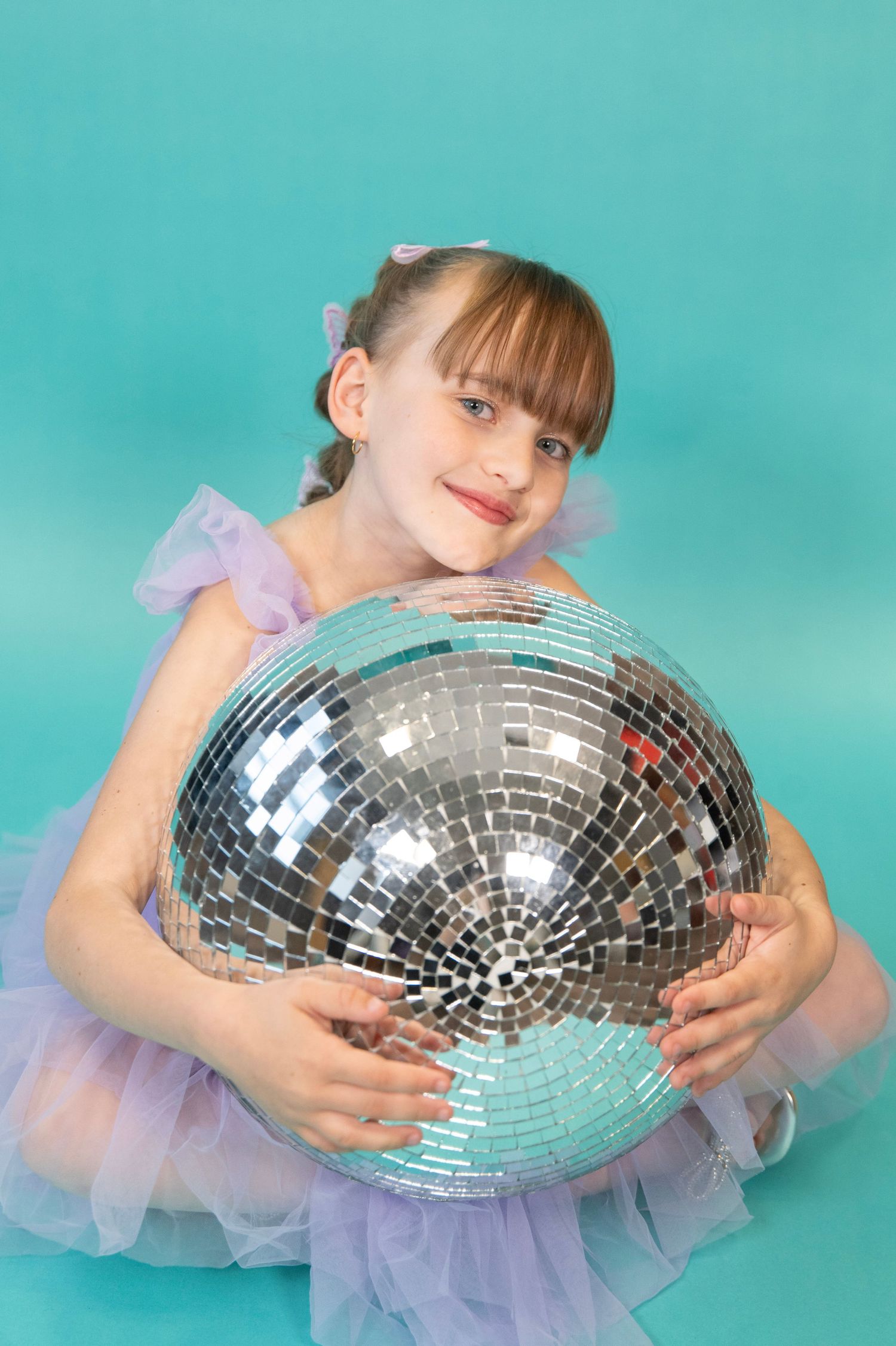 Shiny disco ball held against turquoise backdrop with purple tulle dress details.