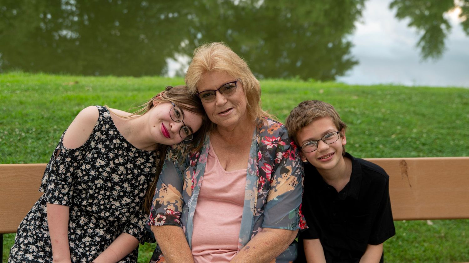 Three people share a moment of laughter while sitting on a bench in a park setting.