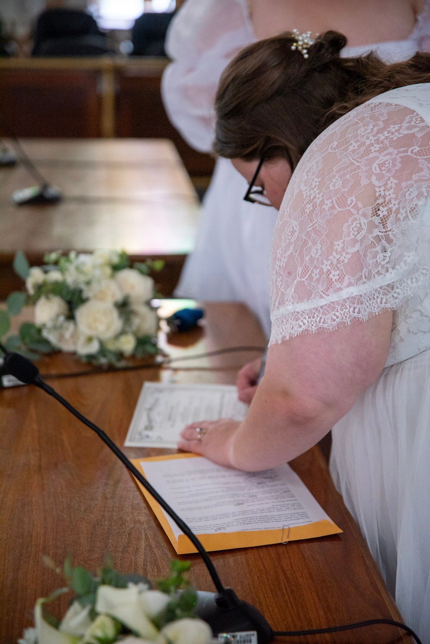 Detailed shots of signing marriage documents with white lace and floral decorations.