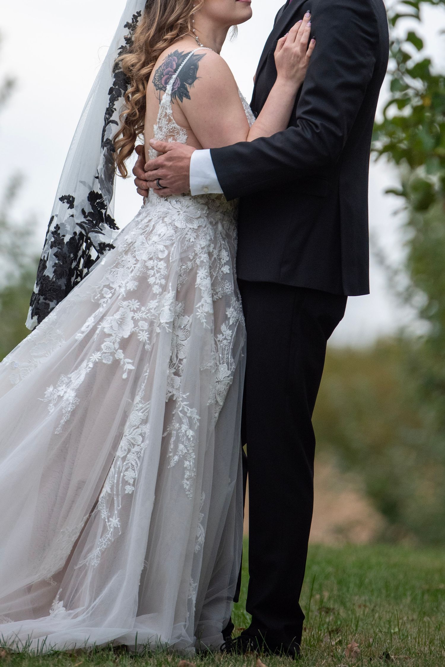 Detail shots of an ornate lace wedding dress against a dark suit in an outdoor setting.