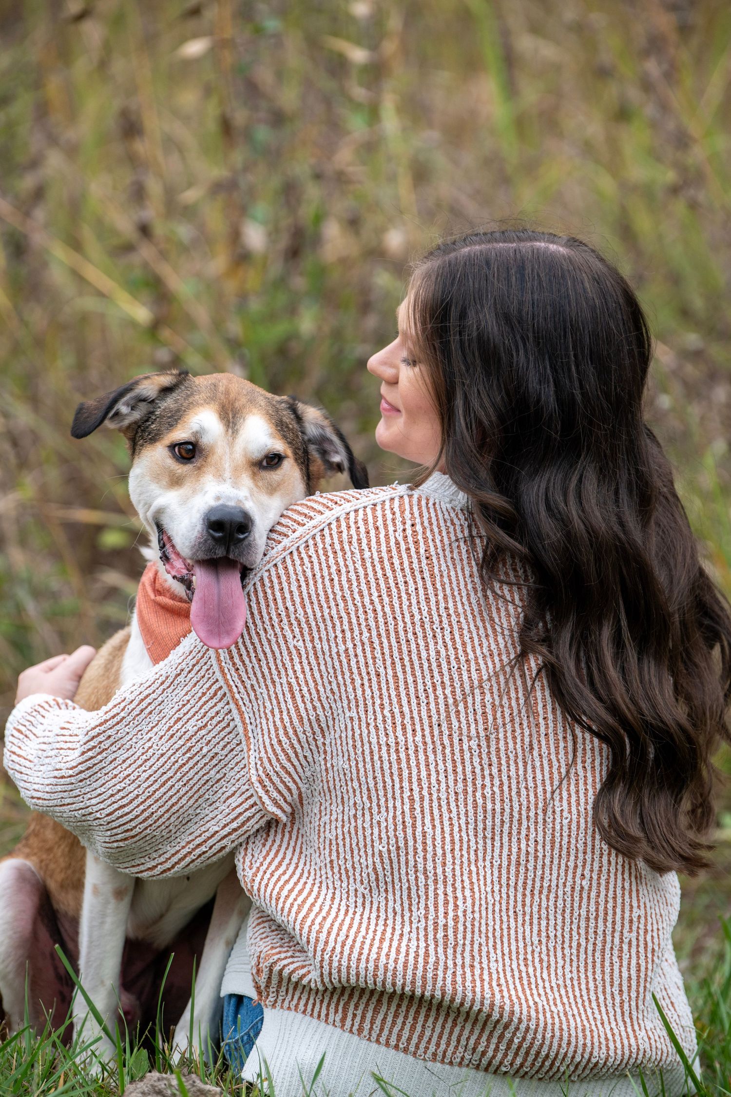 A playful dog leans against someone wearing a beige sweater in an outdoor setting.