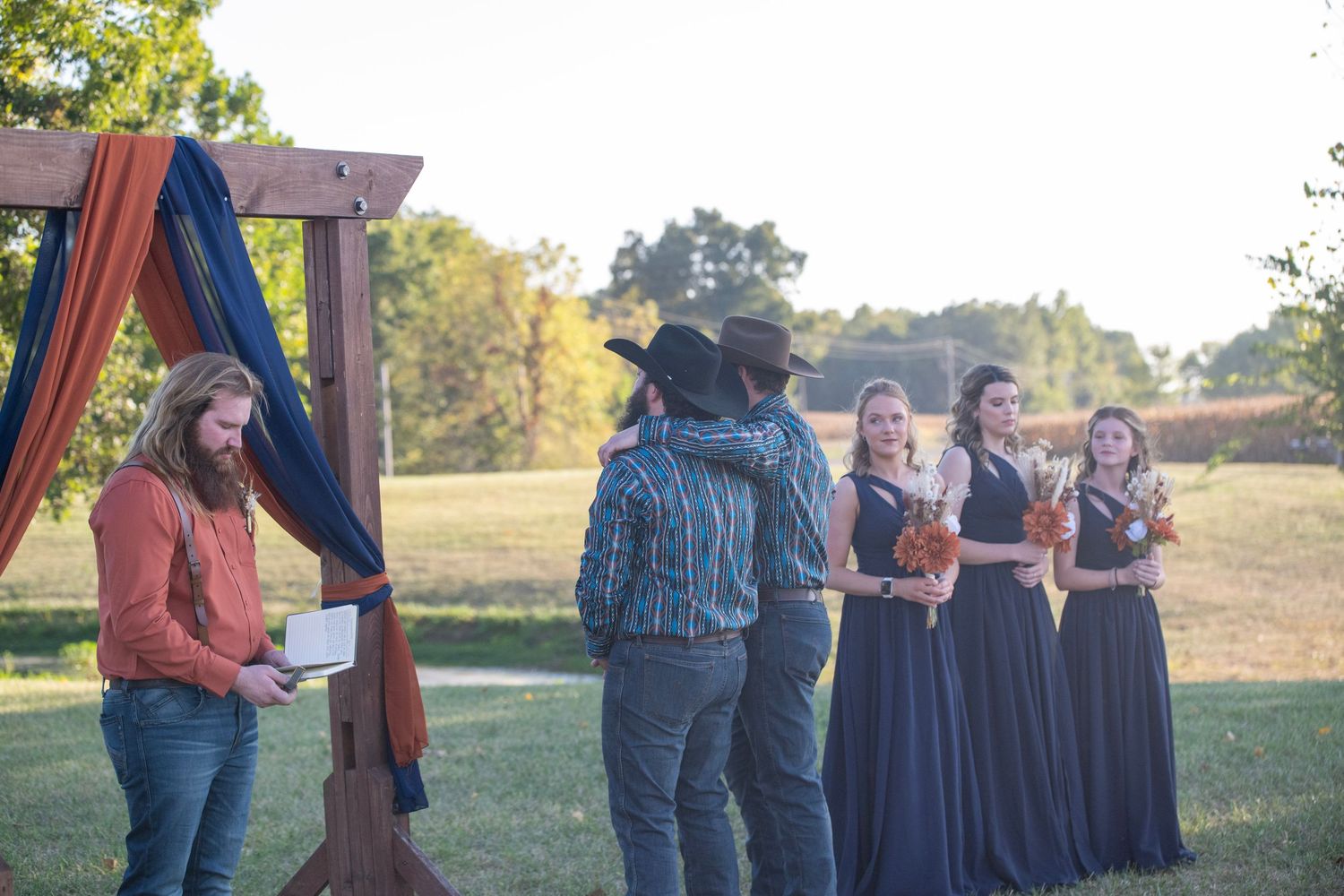 Wedding party members in western and formal attire stand together outdoors.