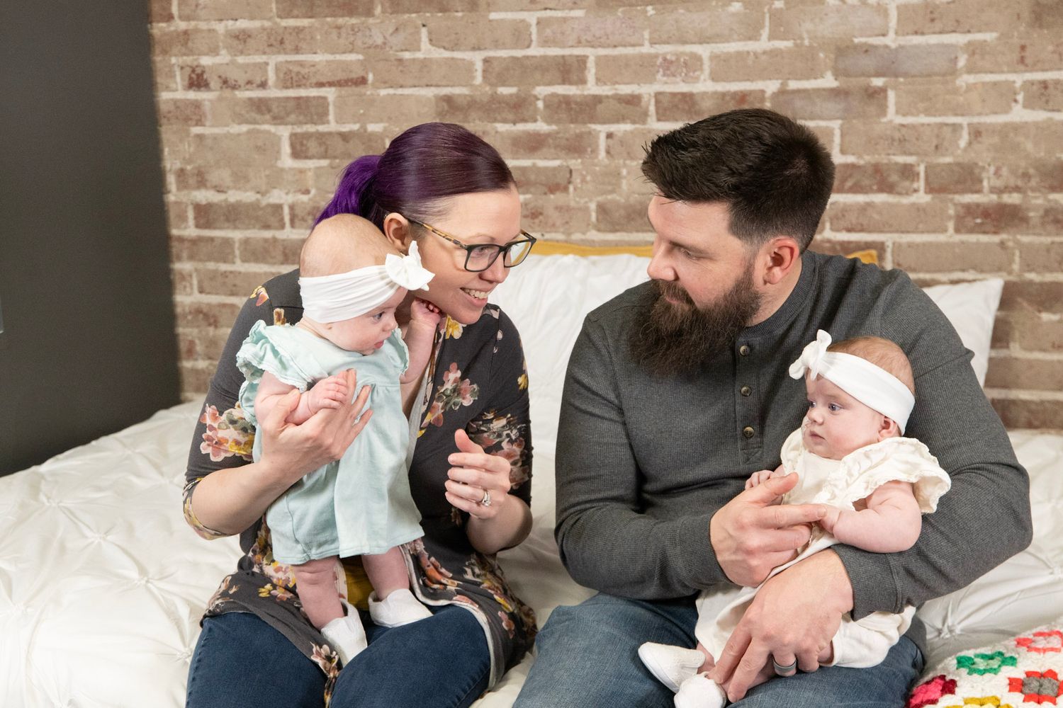 Candid family moment with twins in matching outfits against brick wall backdrop.