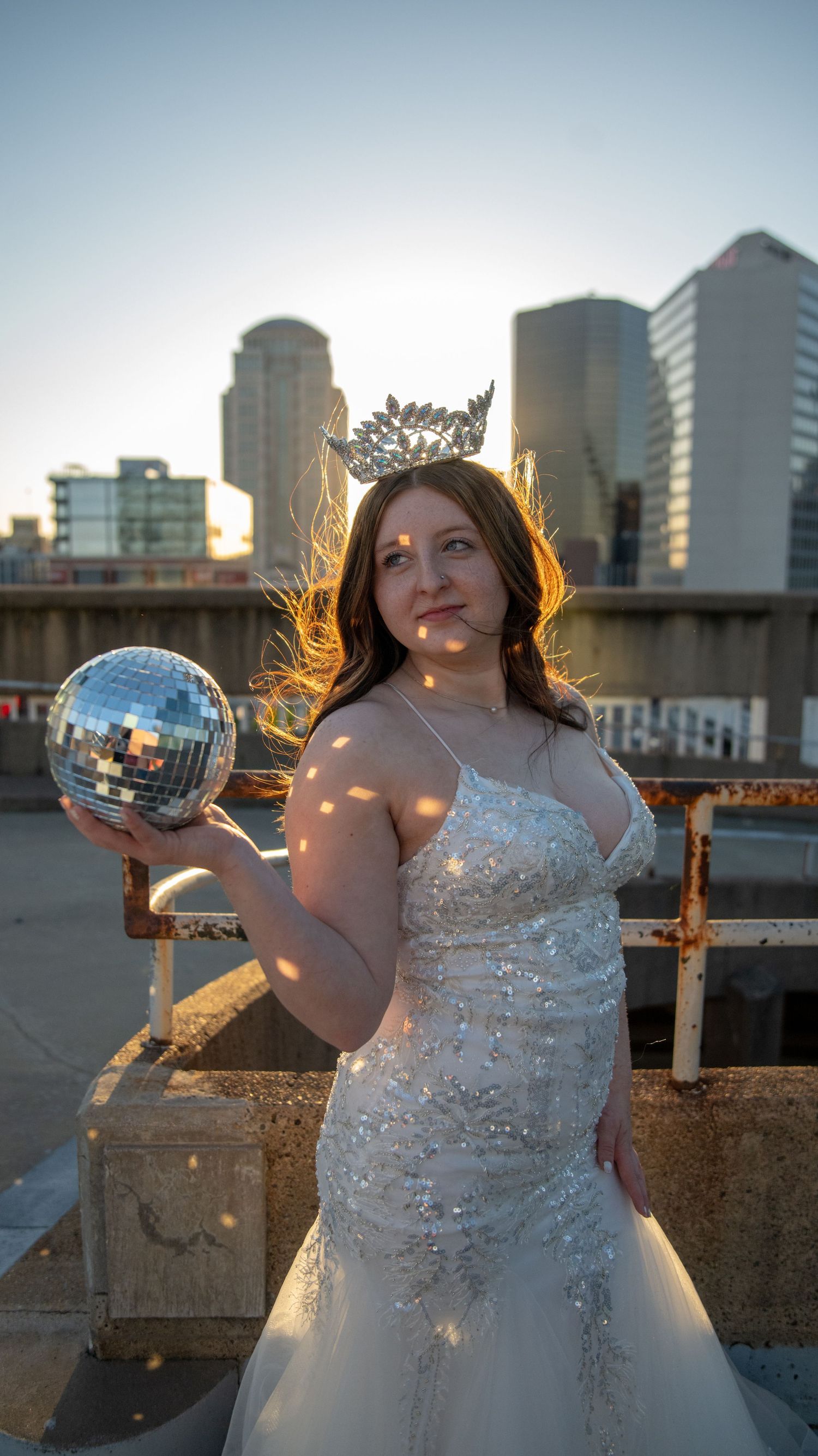 Sunset fashion portraits with a white sparkly dress and disco ball against urban architecture.