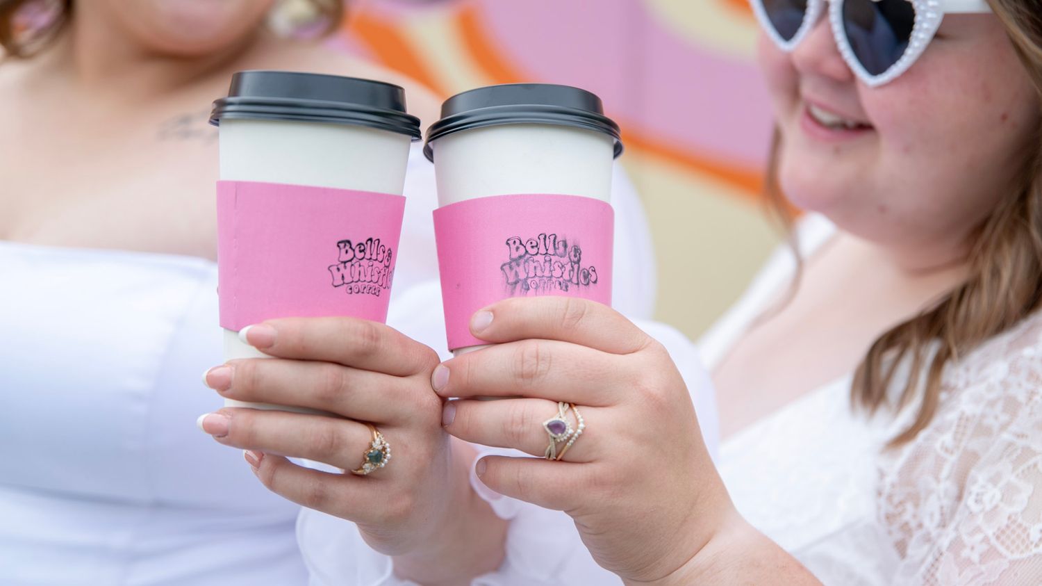 Pink coffee cups being held up against a bright orange background.
