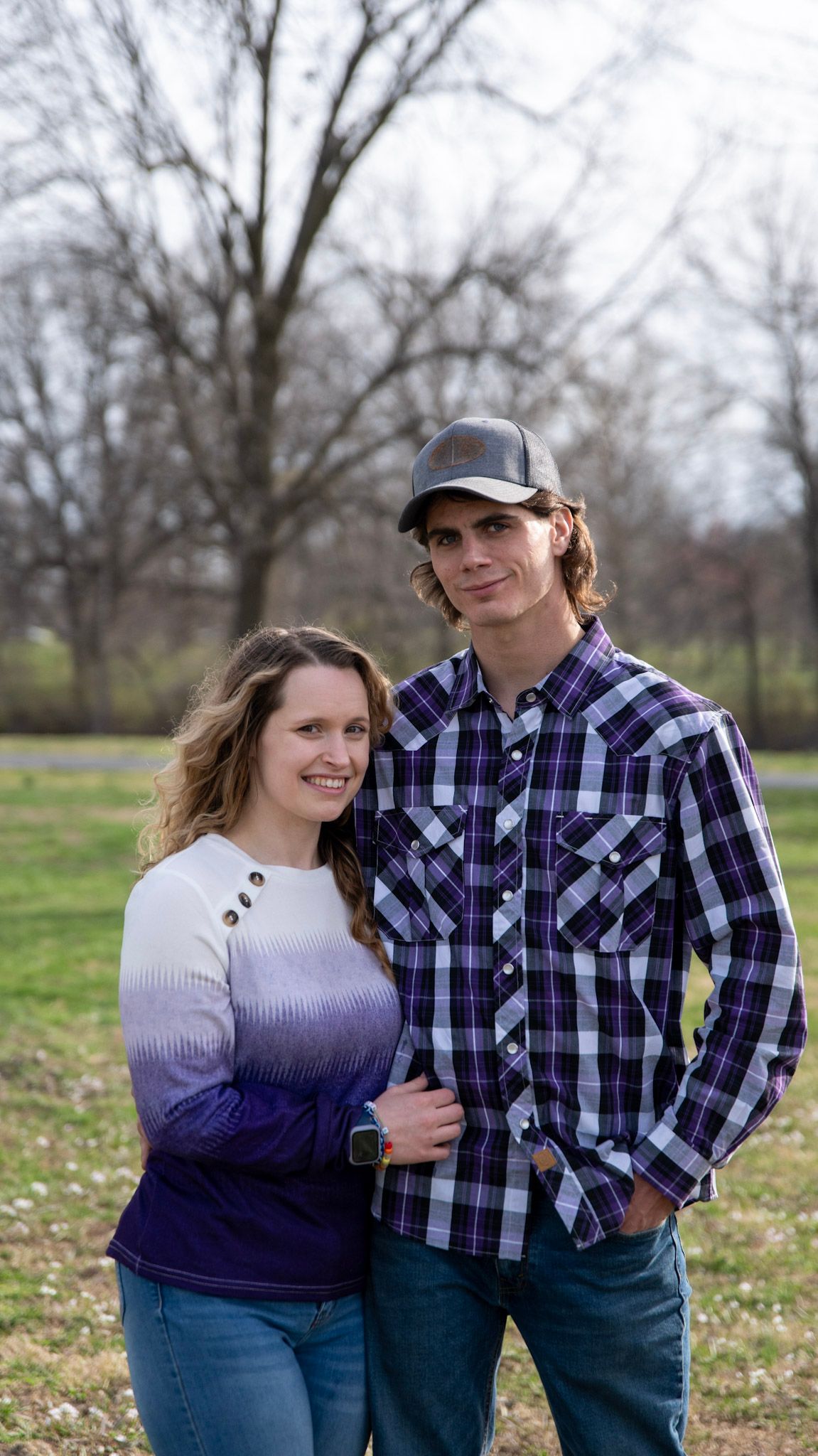 Couple in casual attire posing together outdoors on a spring day.