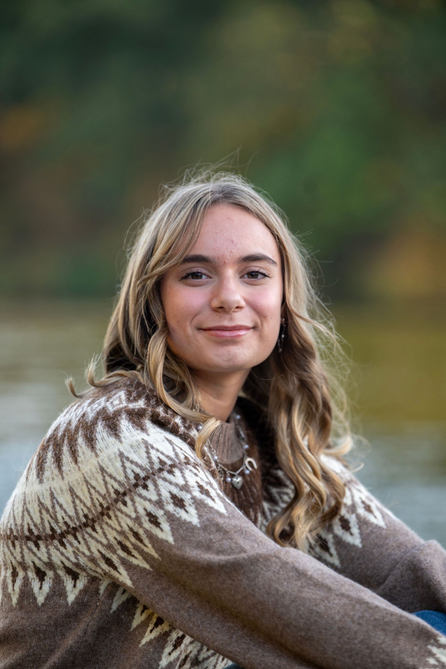 Person wearing cozy brown and white patterned sweater sitting by water.