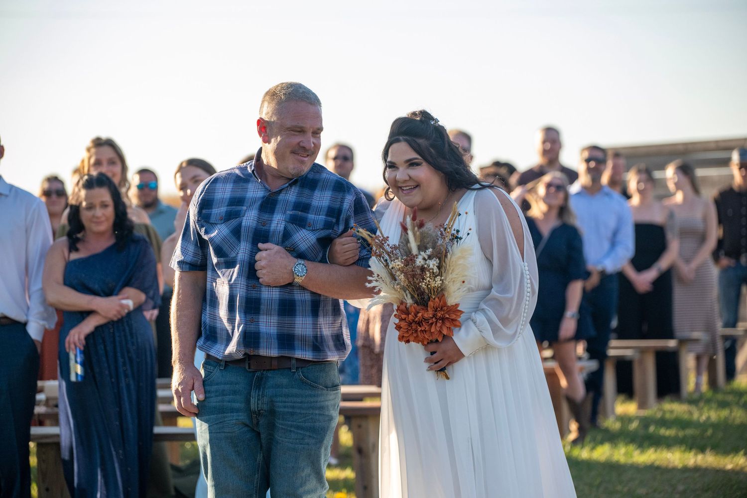 Wedding celebration with guests mingling on a grassy hillside at dusk.