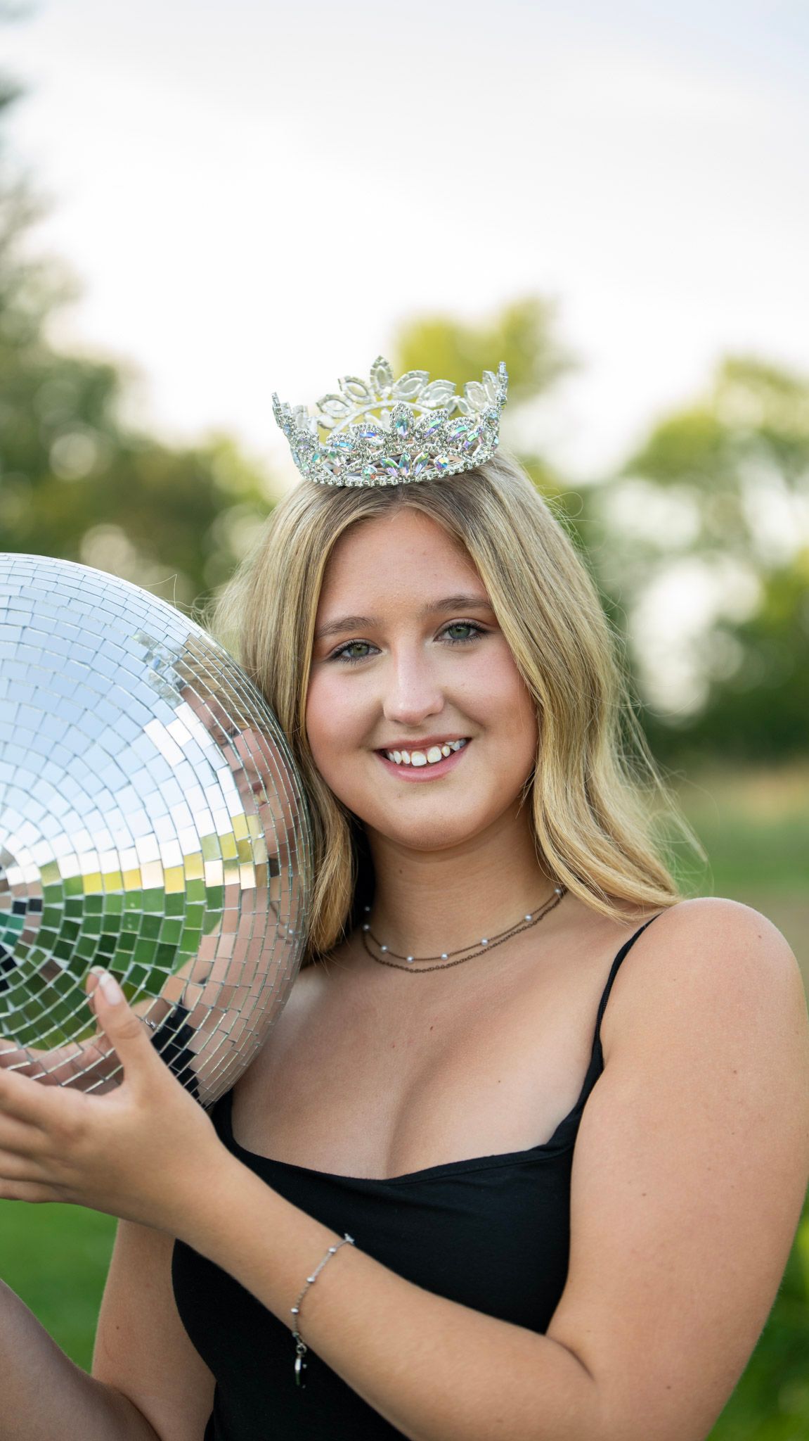 Outdoor portrait with a disco ball and tiara in a sunny field setting.