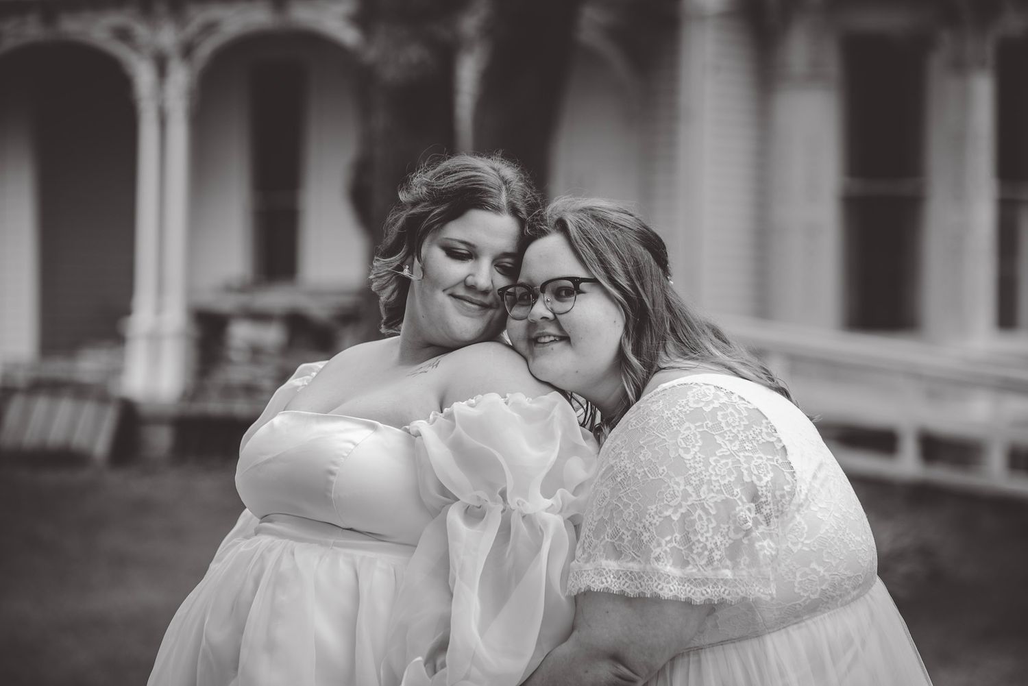 Two people in white wedding attire sharing an intimate moment outdoors.