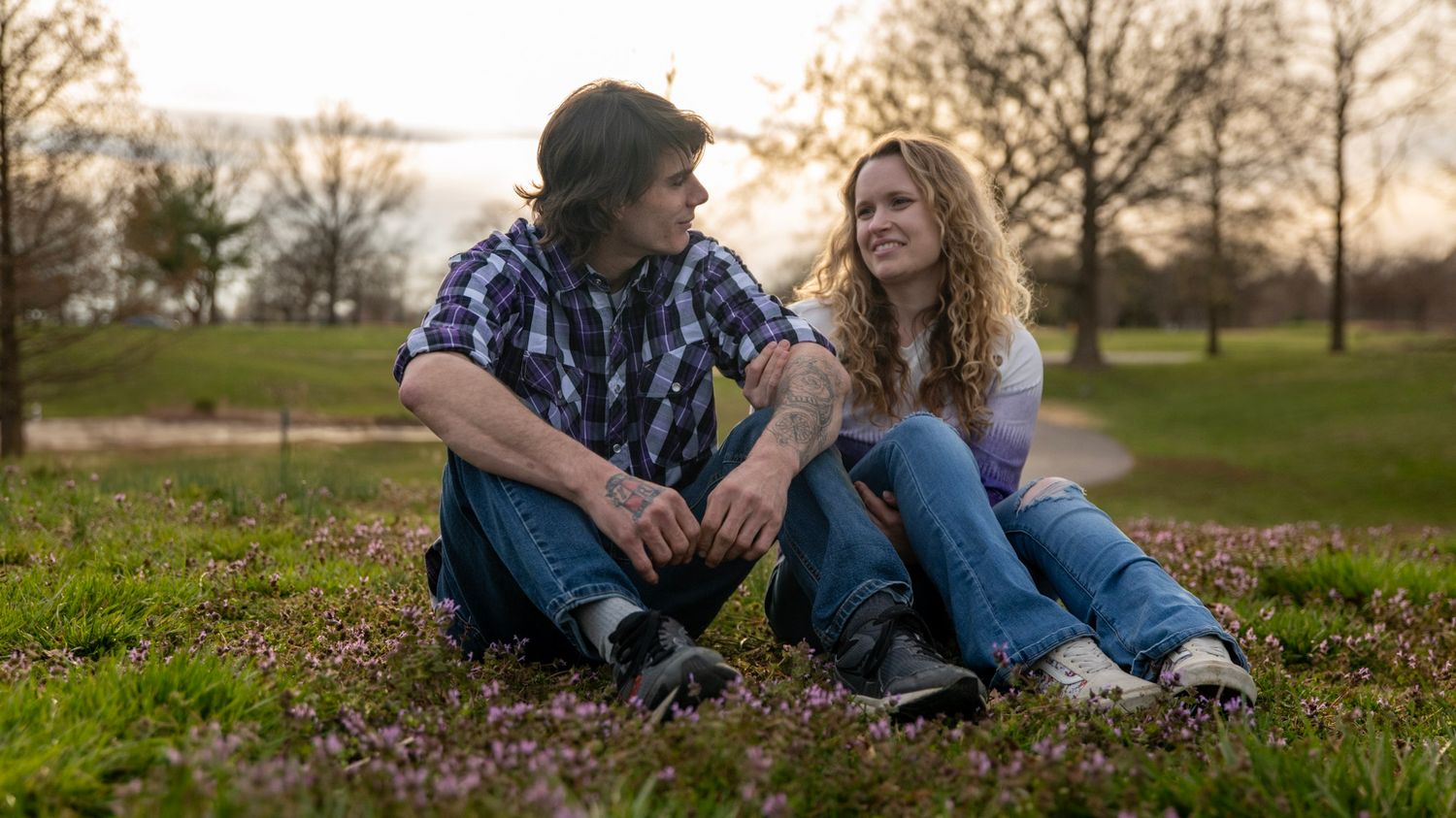 A couple sitting together on grass during golden hour having an intimate conversation.