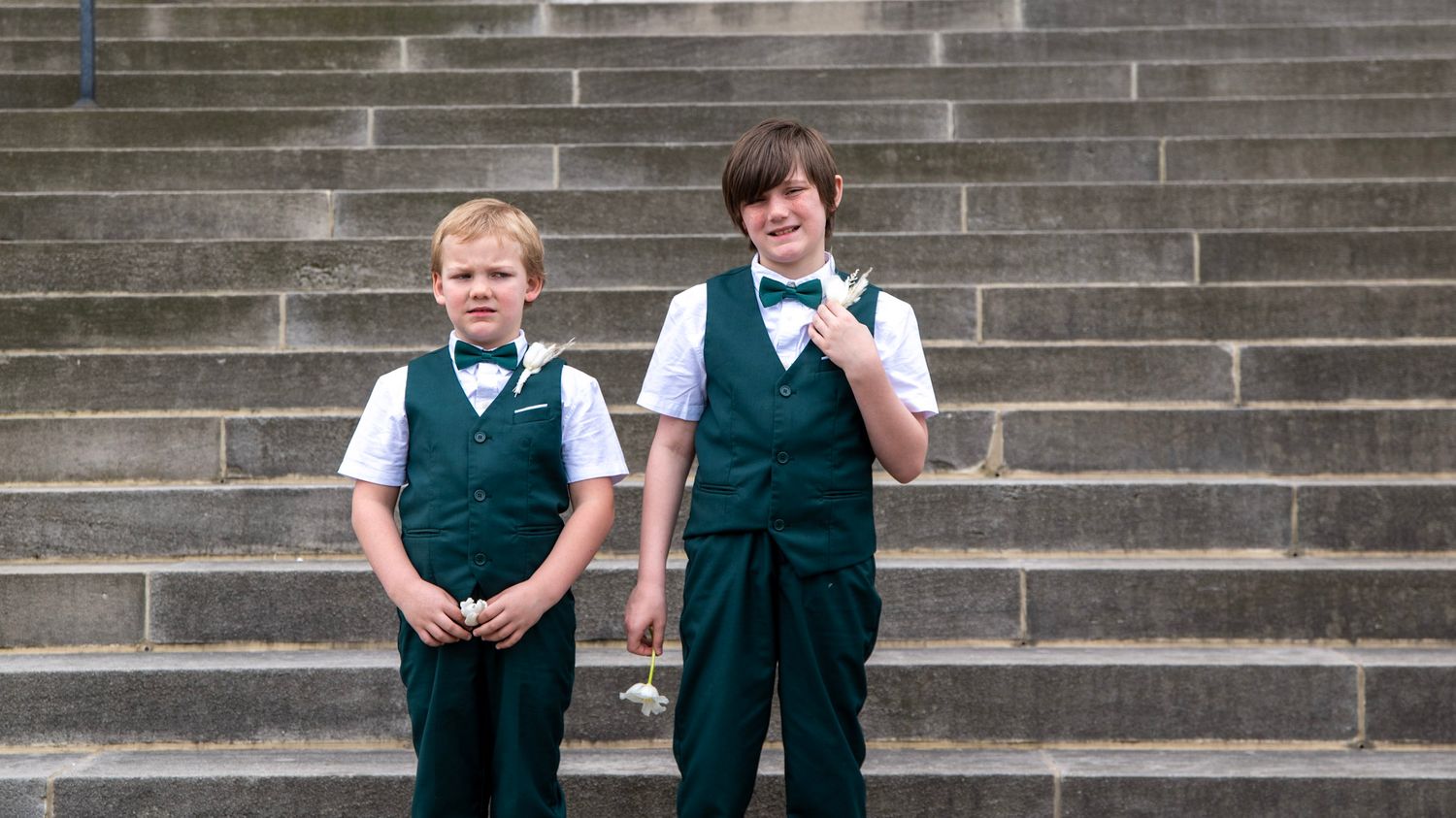 Two young attendants in green vests stand on stone steps outside a building.