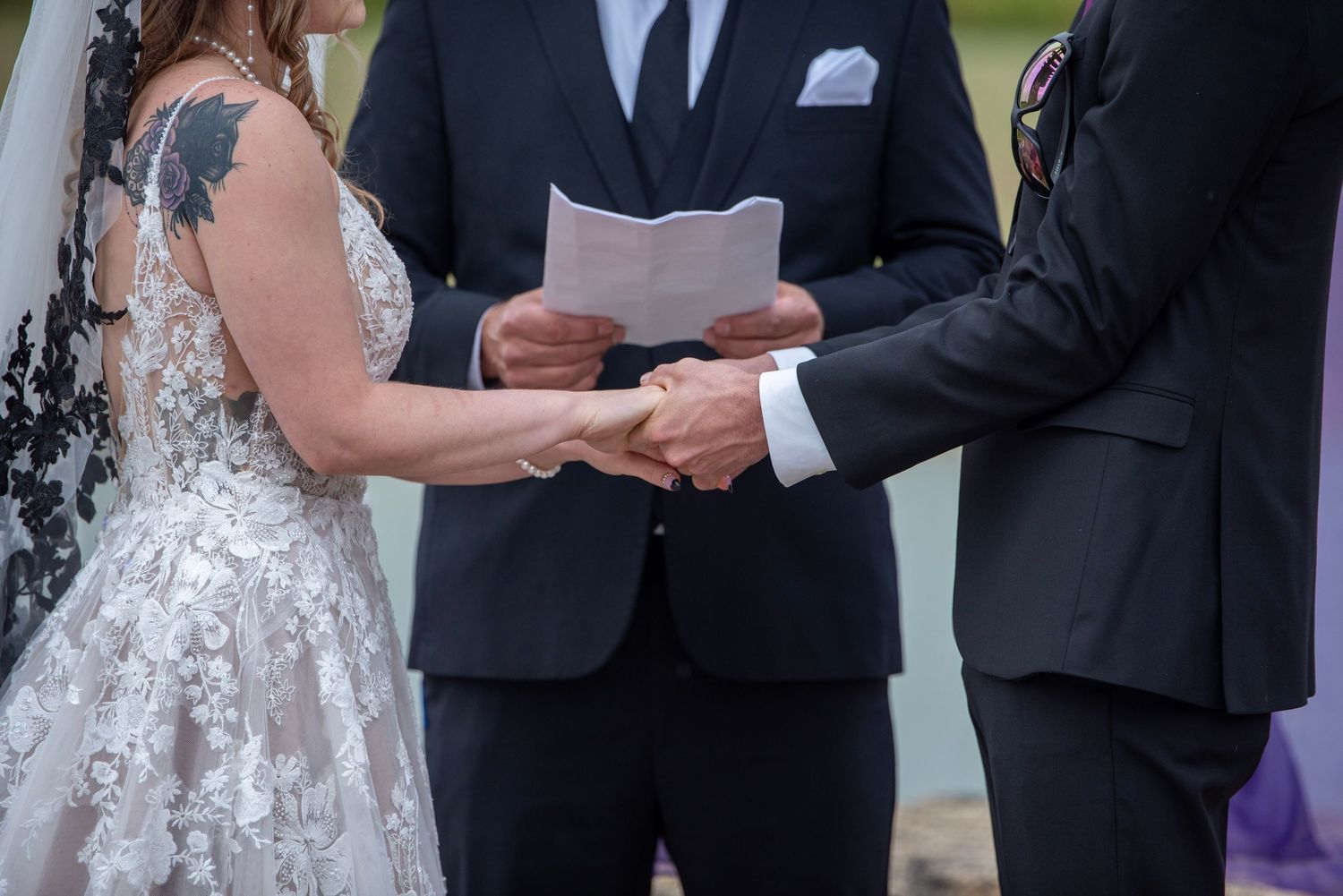 Wedding ceremony participants standing at altar with decorative white and purple backdrop.