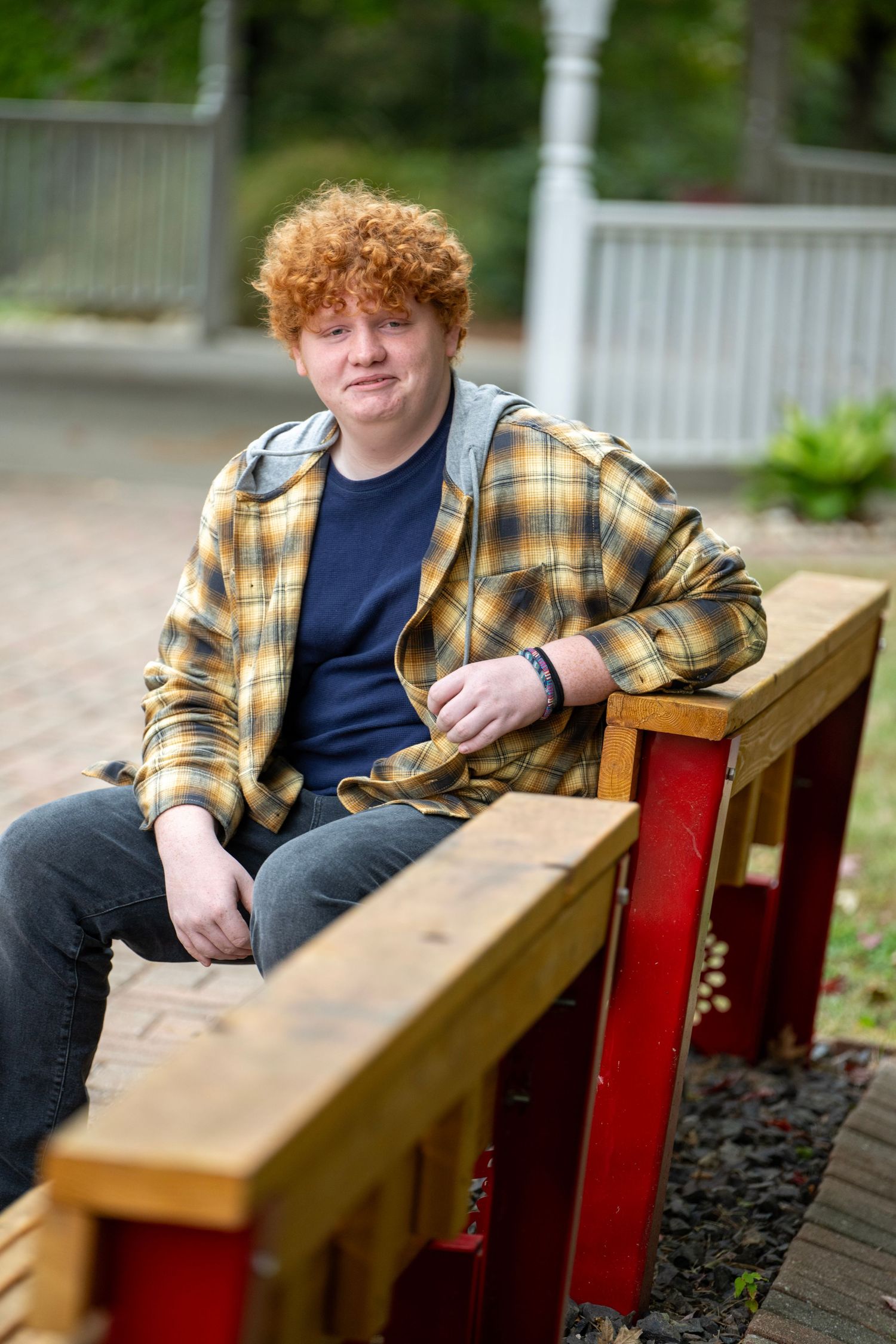 Casual outdoor portrait on wooden bench with white gazebo in background.