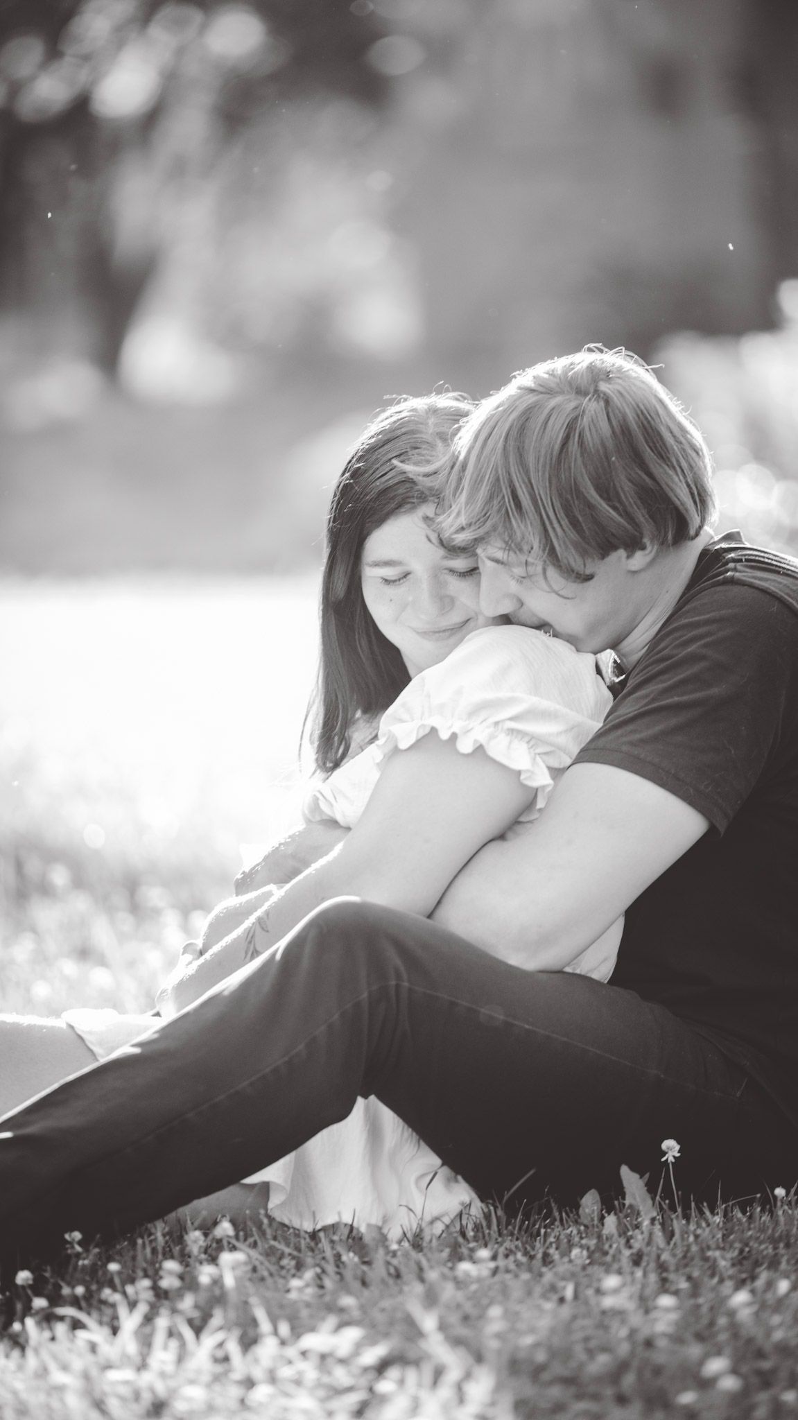 A black and white photo captures an intimate moment between a couple sitting in grass.