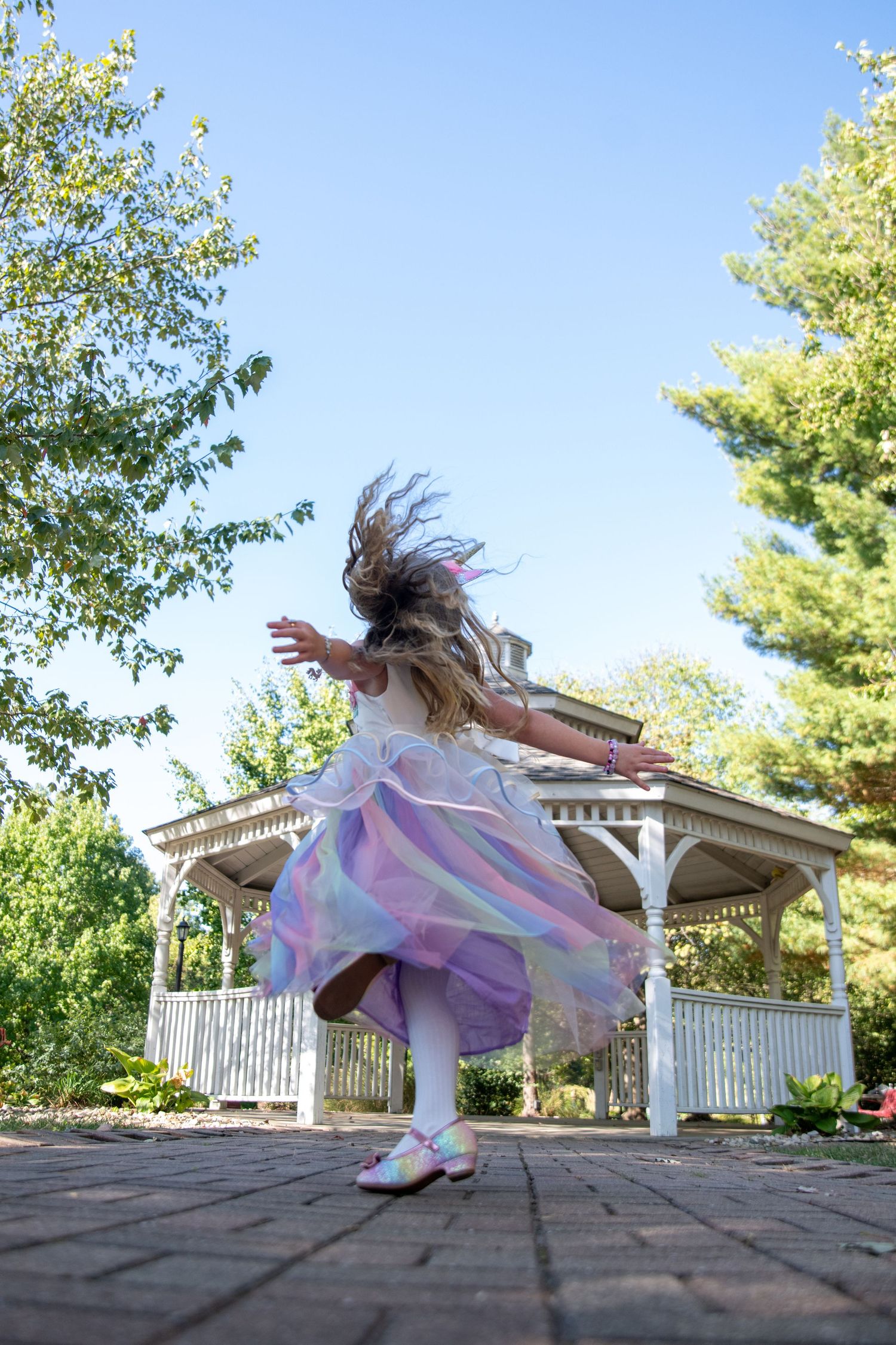 Dynamic action shots of a child leaping and dancing on brick pavers near a white gazebo.
