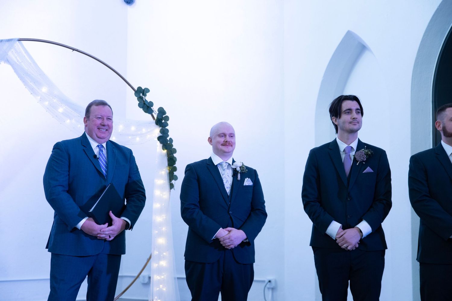 Groomsmen lined up in black suits during wedding ceremony in church.