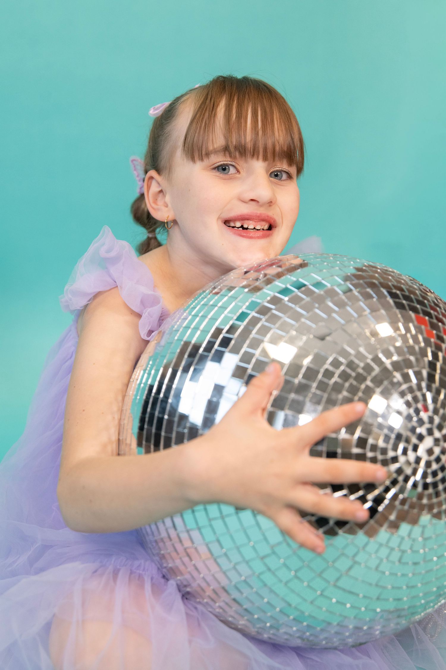 Large disco ball being held against turquoise studio backdrop.