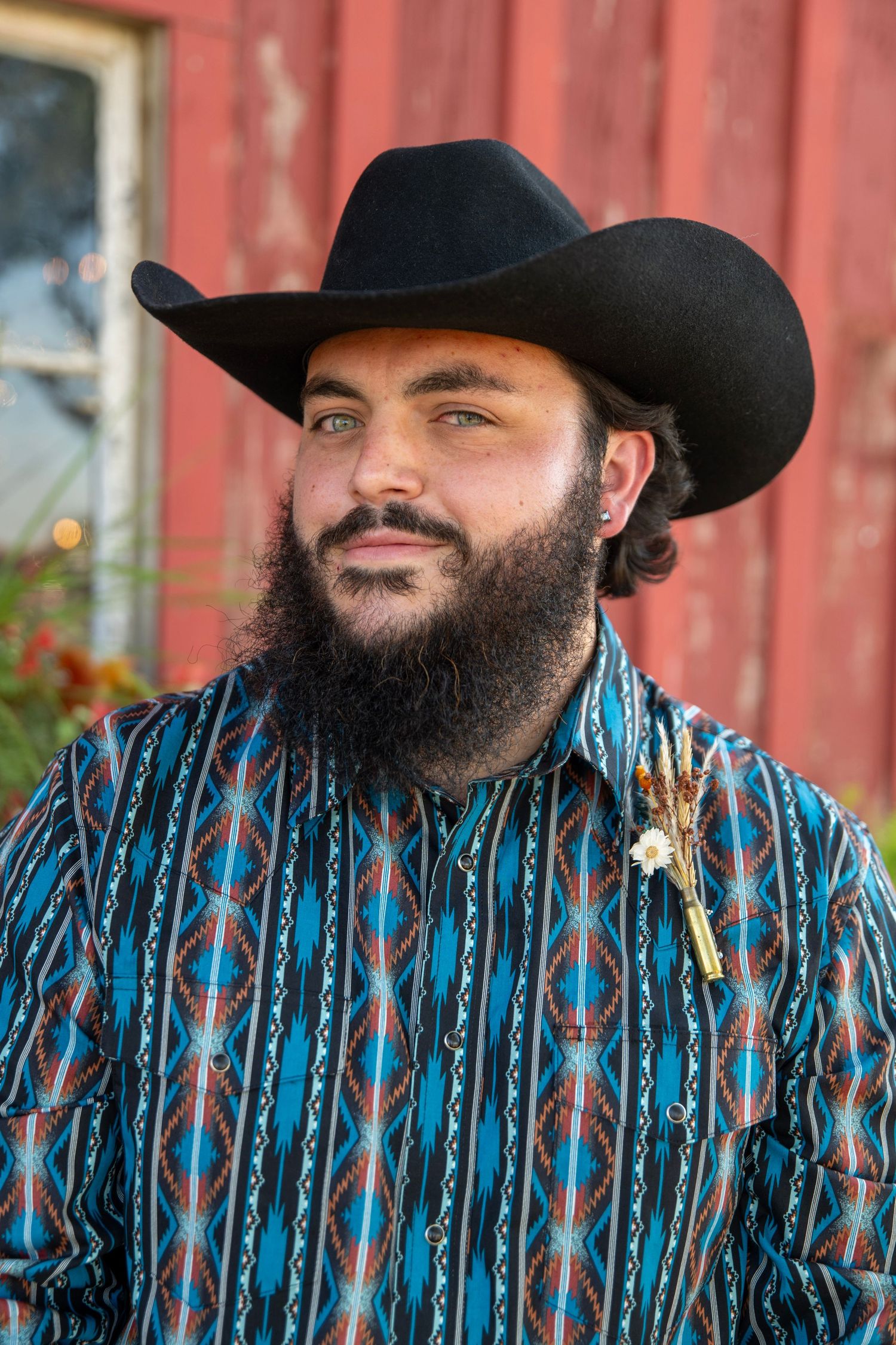 Person wearing black cowboy hat and blue patterned shirt smiles against red barn backdrop.