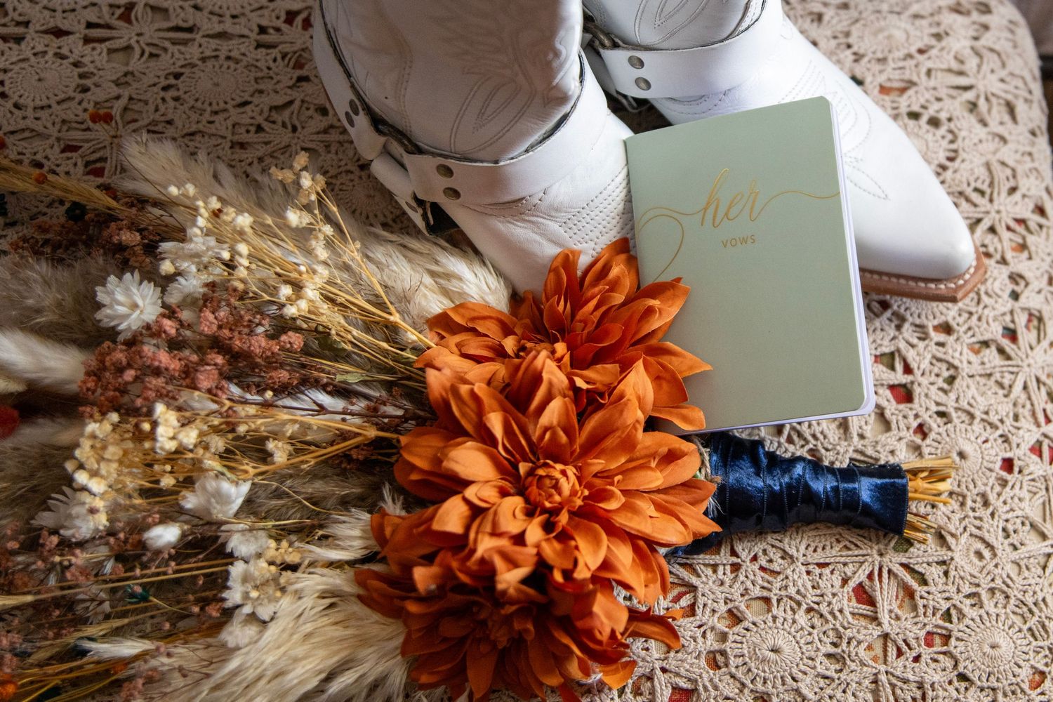 Wedding accessories including white shoes, orange flowers, and a mint green book on lace fabric.