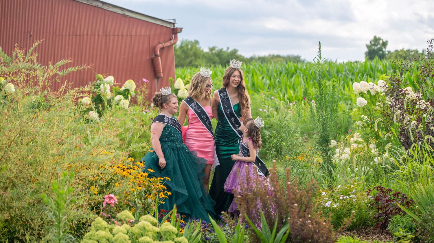 Group photo taken in a garden landscape with colorful flowers and a red barn in background.