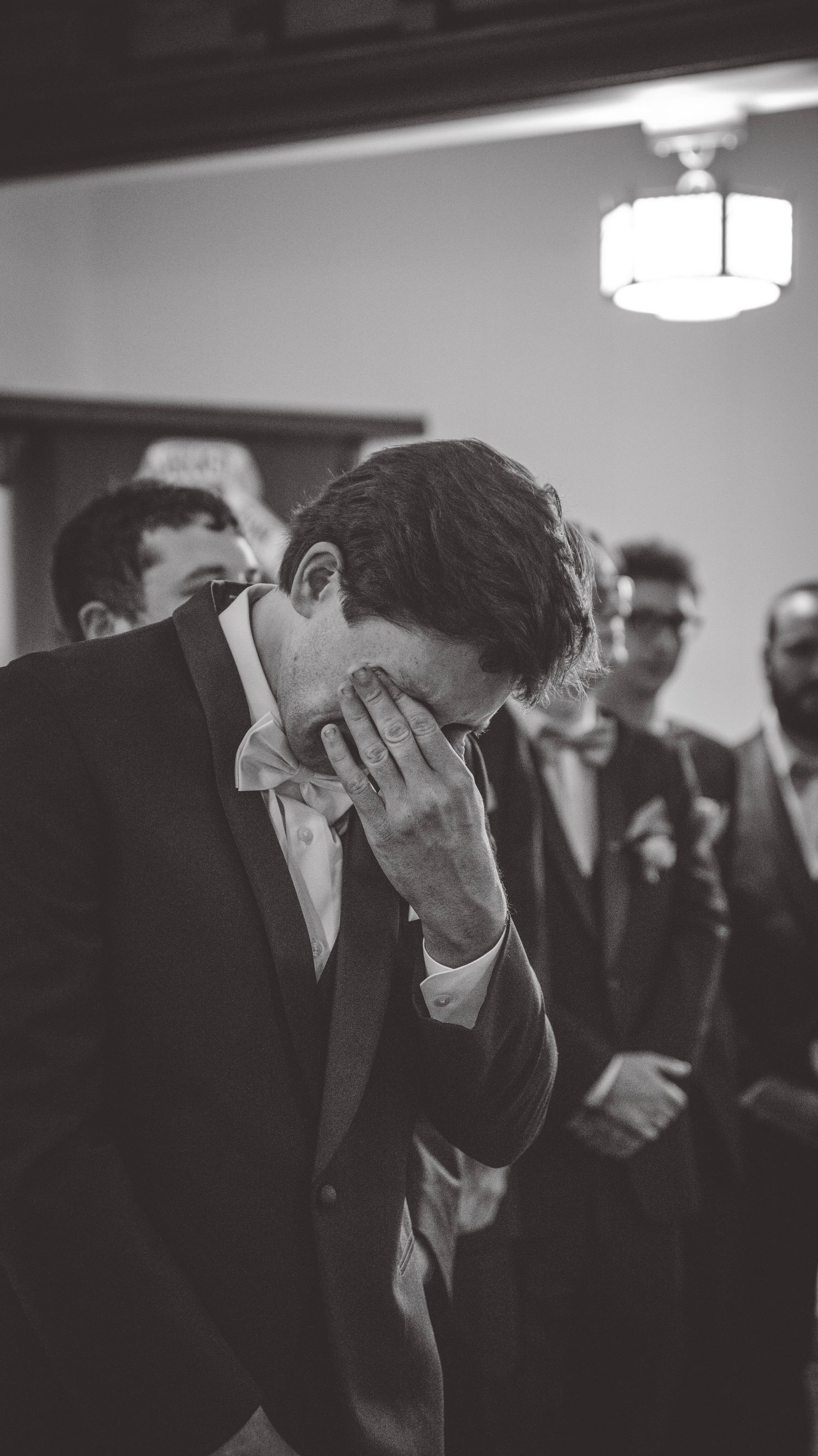 Emotional moment captured in black and white as groomsmen wipe tears at wedding ceremony.