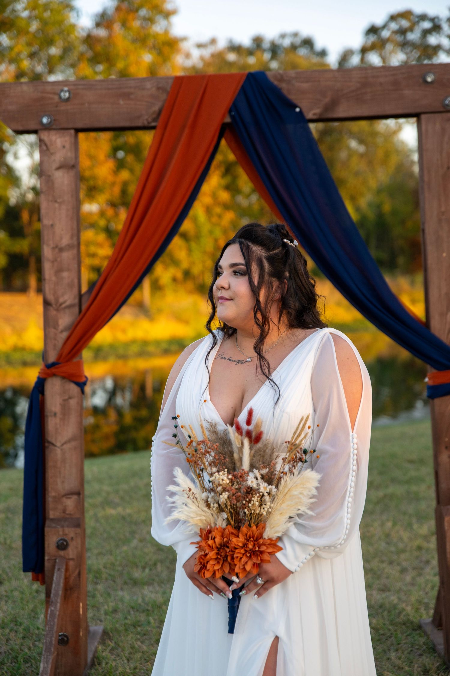 White wedding dress contrasts against wooden arch draped with navy and rust fabric during autumn ceremony.