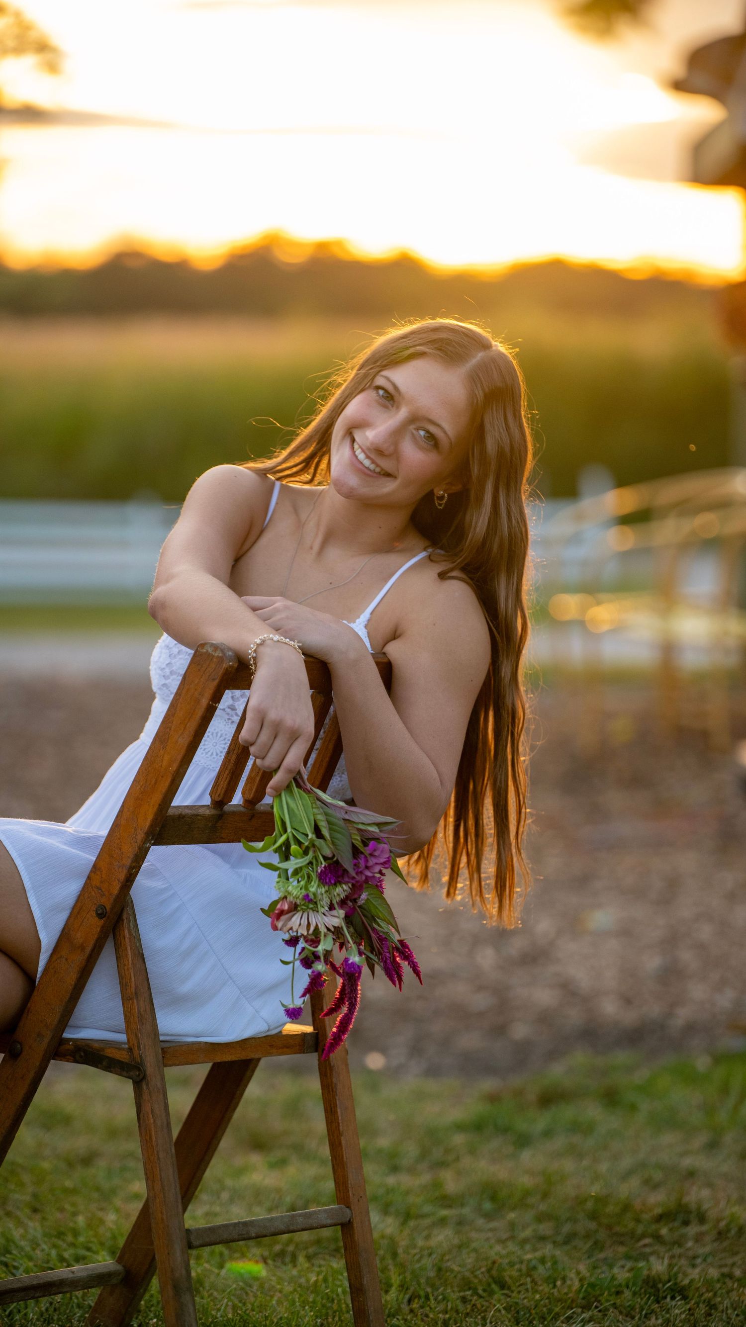 A white sundress photoshoot at golden hour with a wooden chair and wildflowers in a rustic outdoor setting.