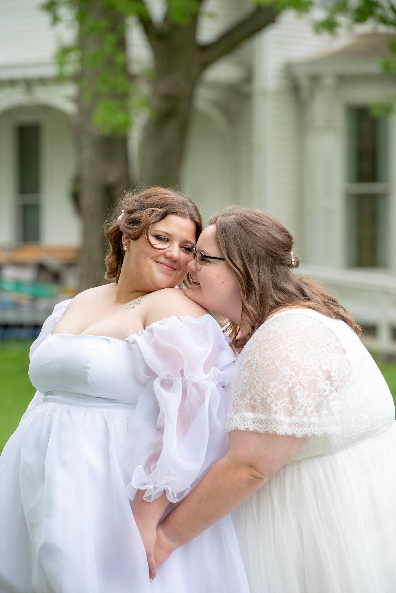 Two people in white wedding gowns sharing a tender moment in a garden setting.