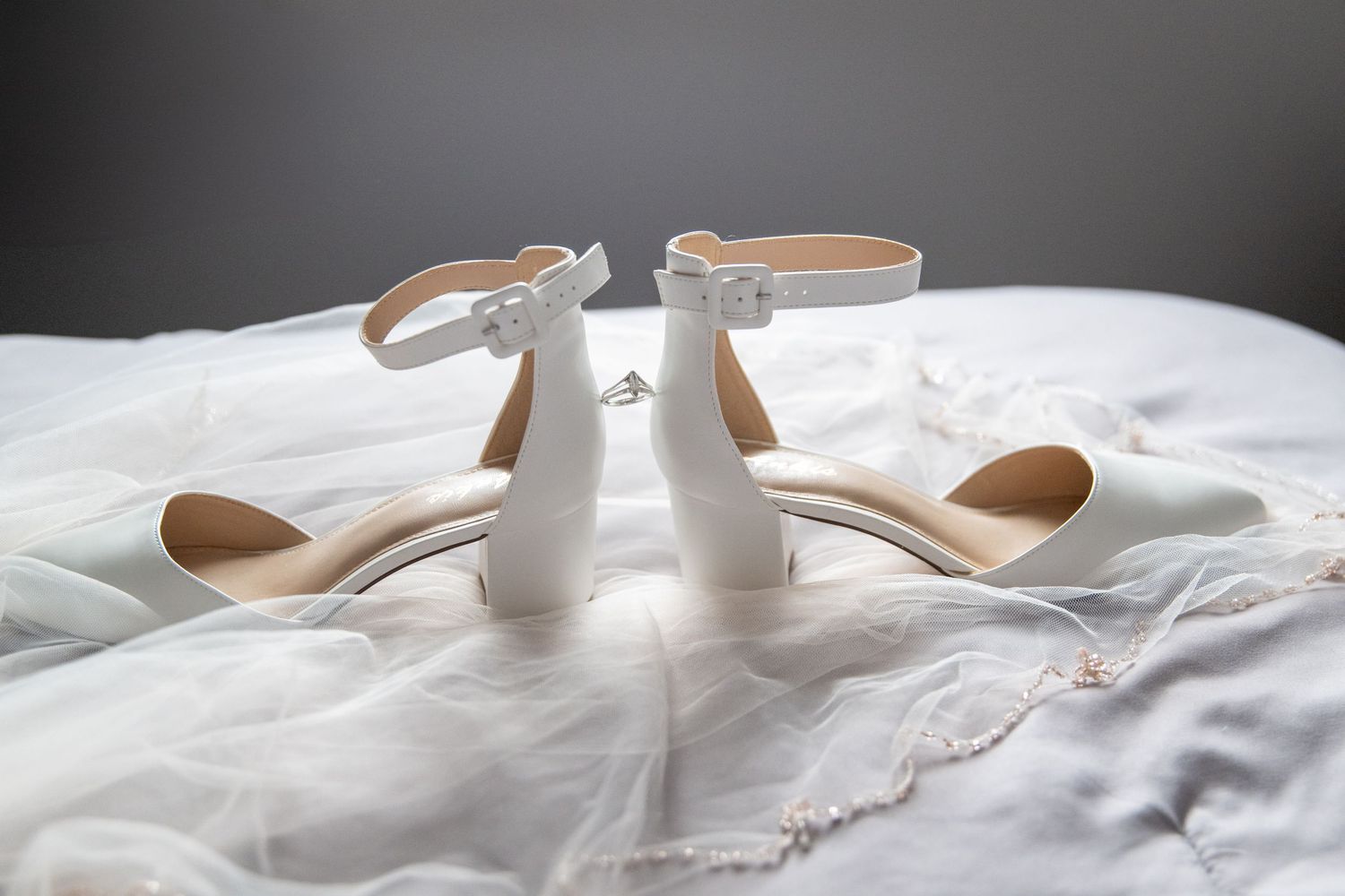 Elegant white bridal shoes displayed on soft white fabric with delicate details.