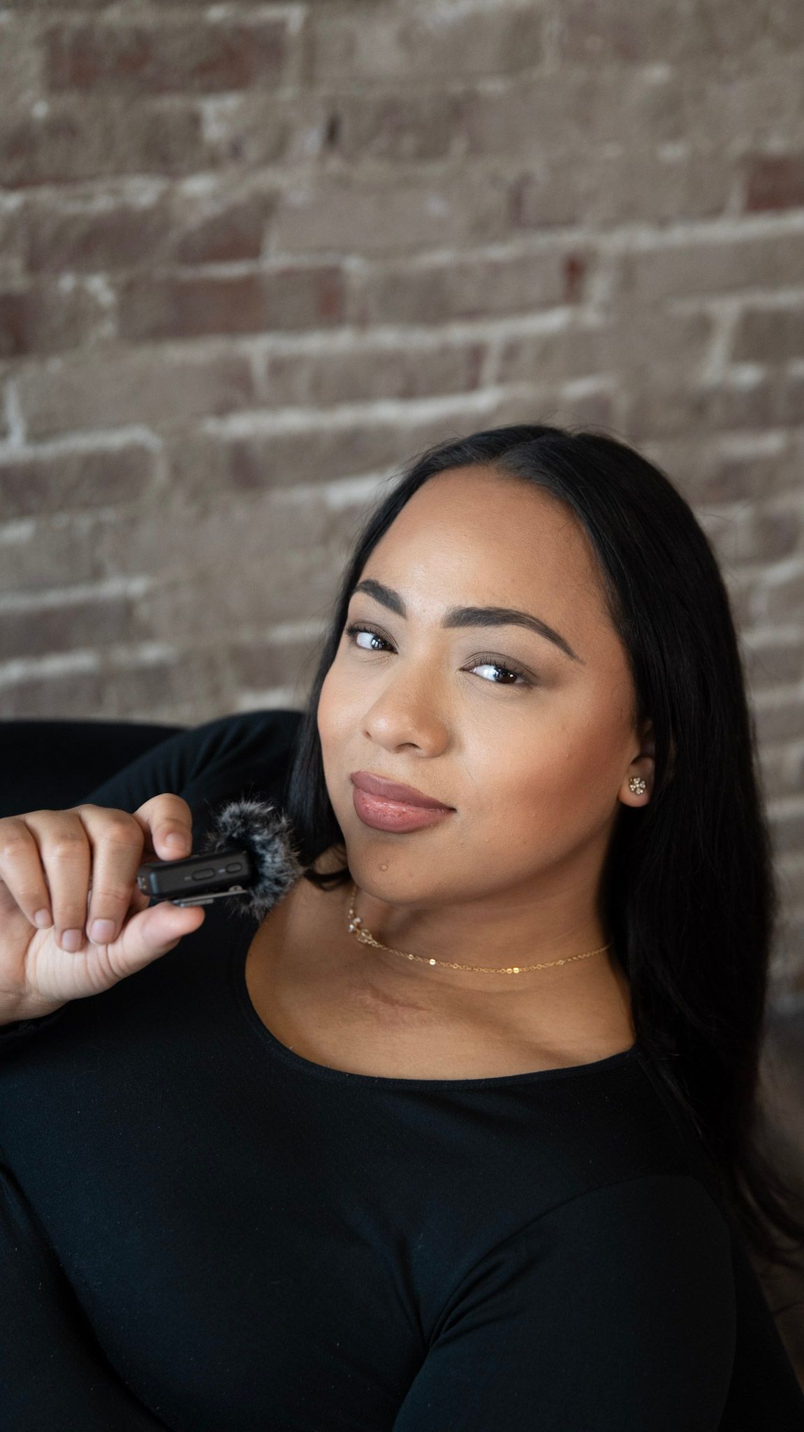 Woman in black top posing against rustic brick wall background.